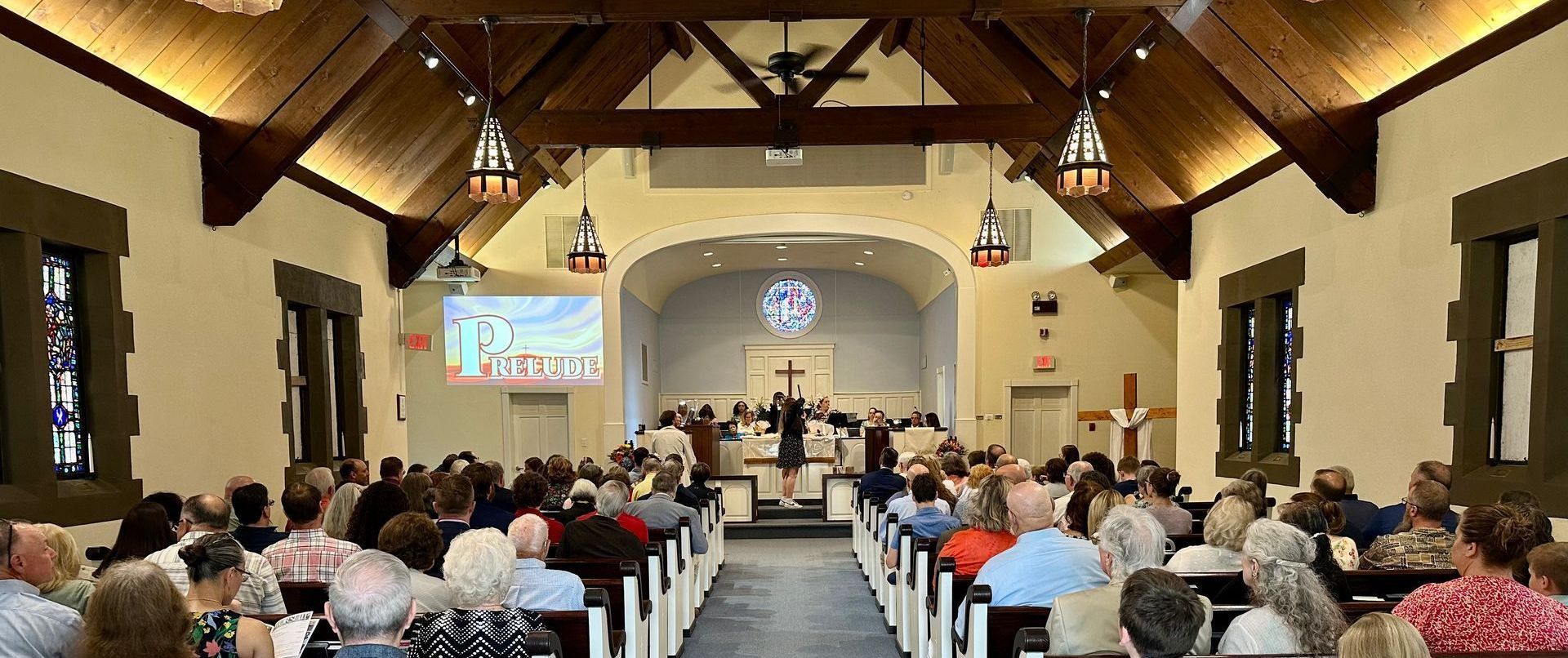 Interior of a church with people seated in pews, looking toward the altar and a presentation screen.