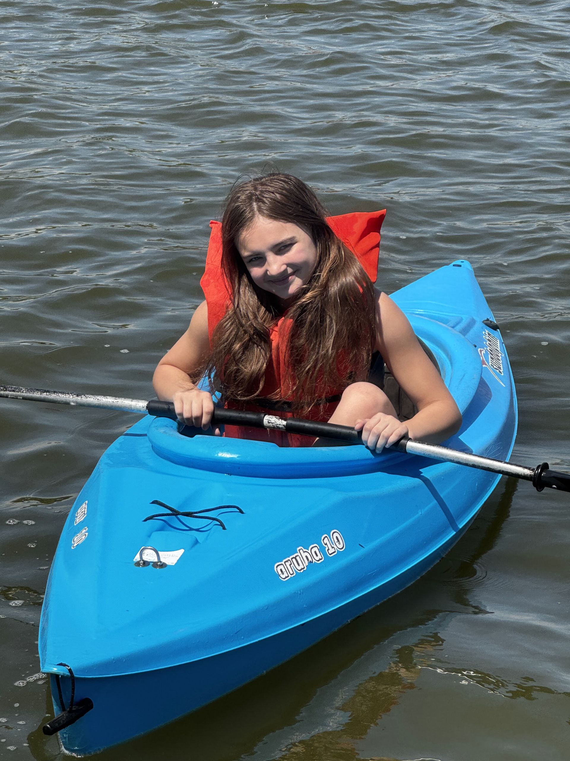 Person smiling in a blue kayak on calm water, holding a paddle.