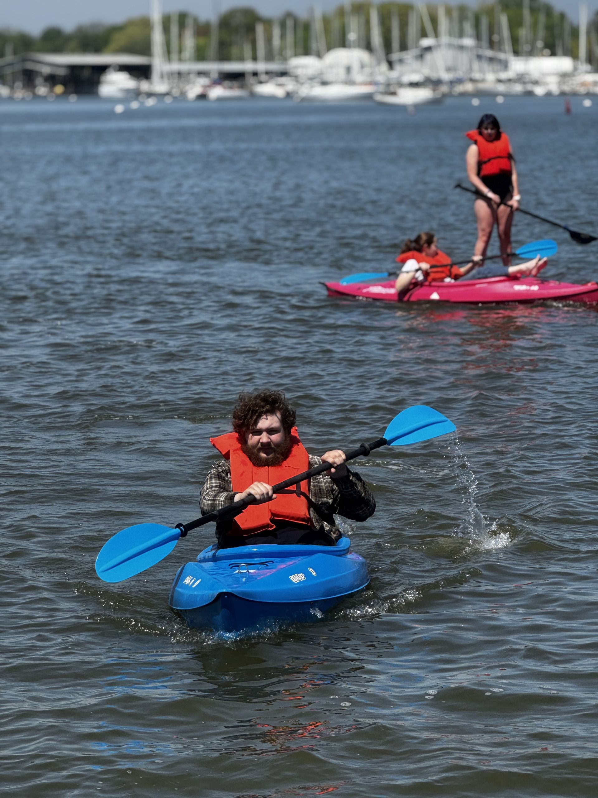 Two kayakers in life jackets paddling on blue and pink kayaks on a calm marina