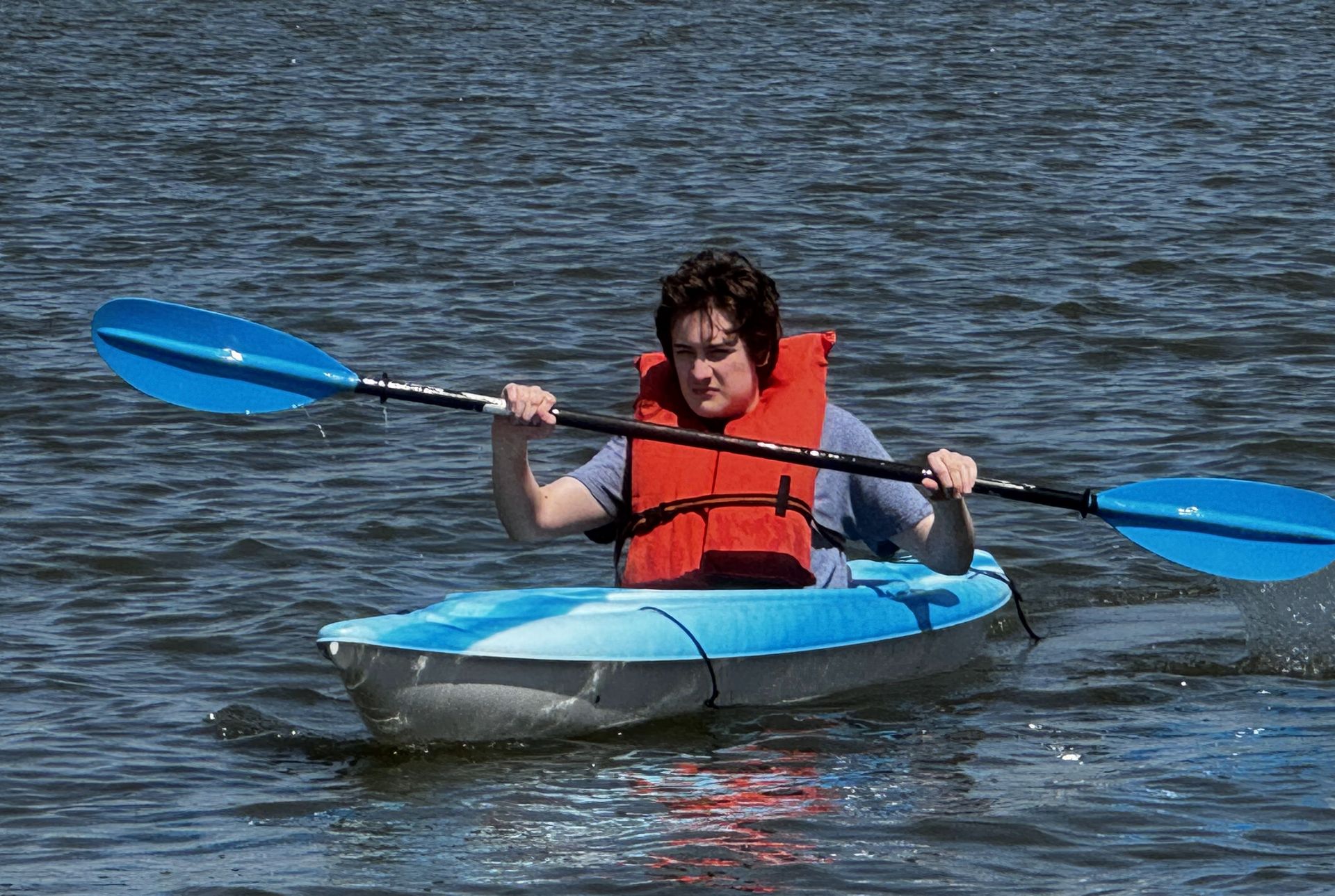 Person in a red life jacket kayaking on calm water with a blue paddle