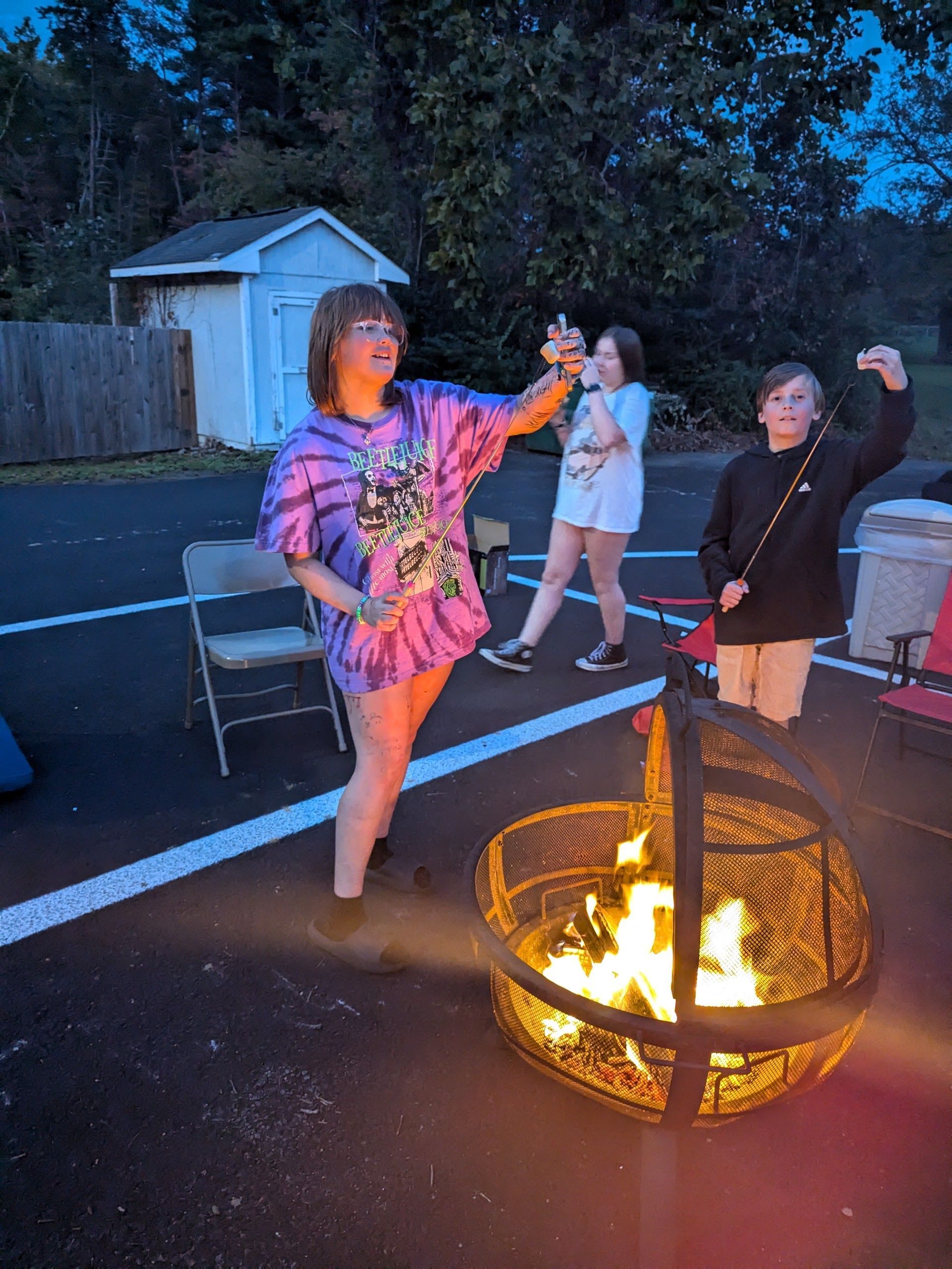 People roasting marshmallows over a bonfire in an outdoor setting at dusk.