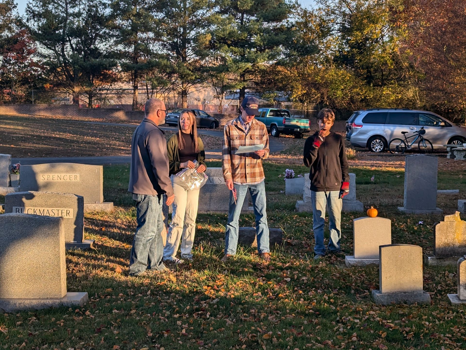 People gathered in a cemetery in front of headstones on a sunny day.