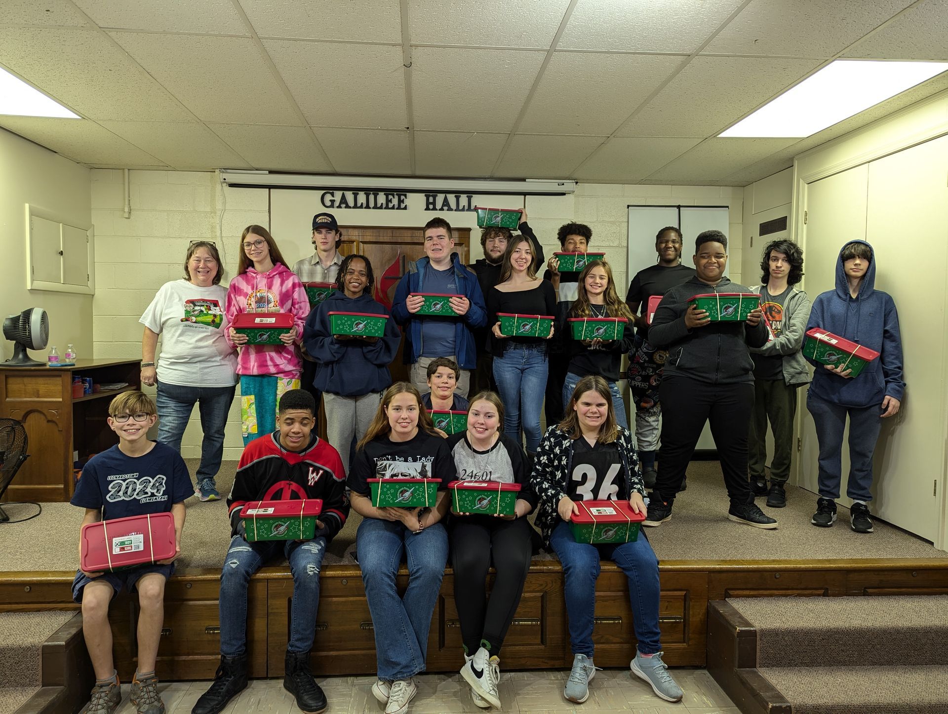 Group of teens in Galile Hall, holding decorated gift boxes.