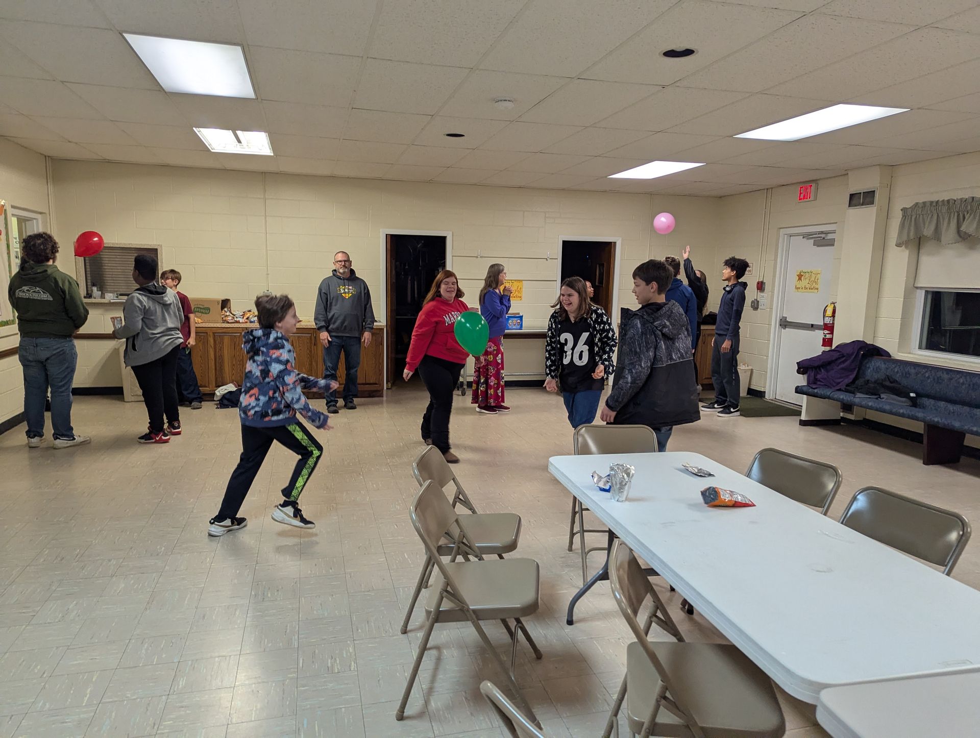 People in a room playing with balloons. A child throws a ball, other people watch.