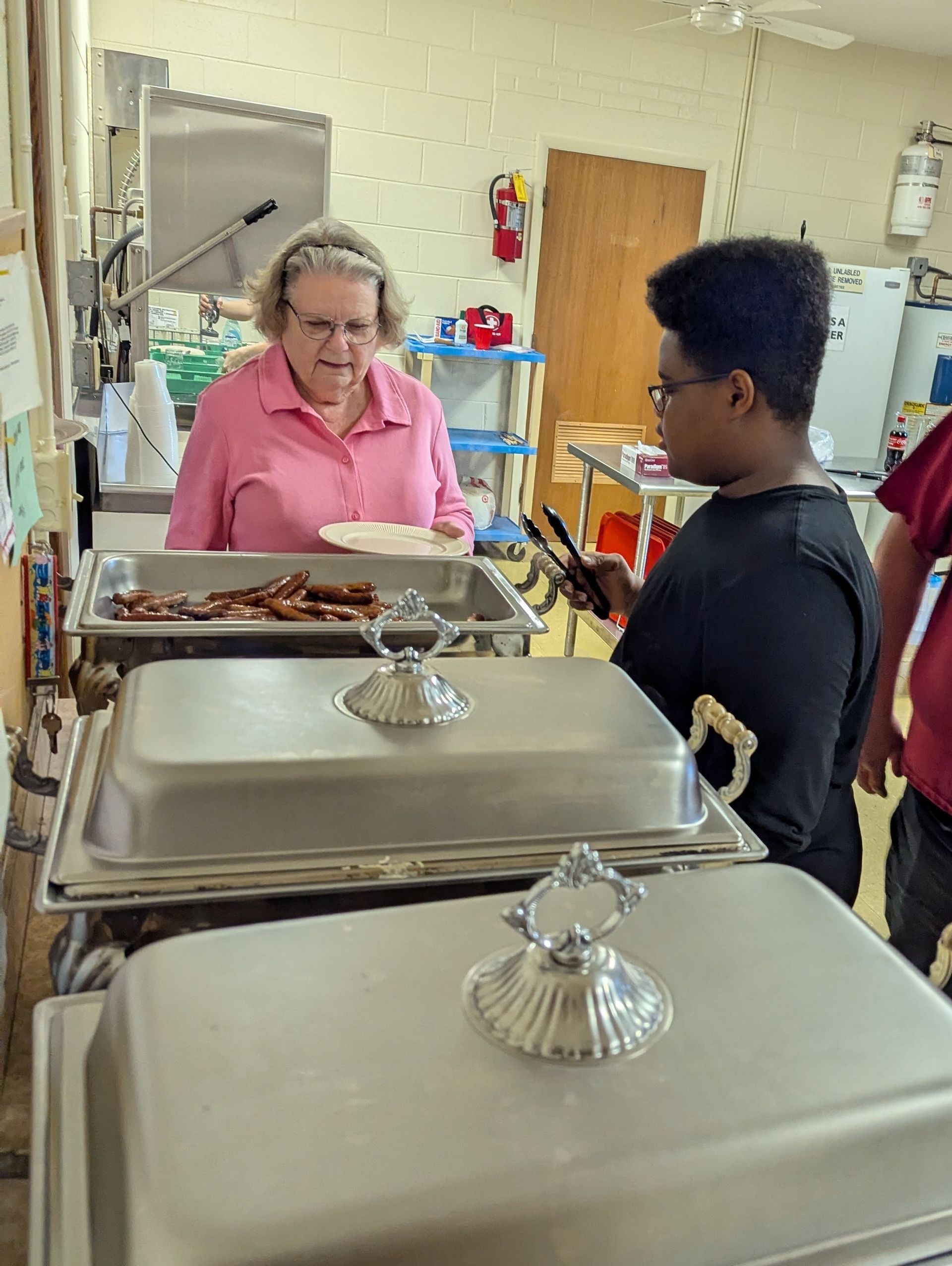 Woman in pink shirt serves food to a person with dark hair at a buffet table.