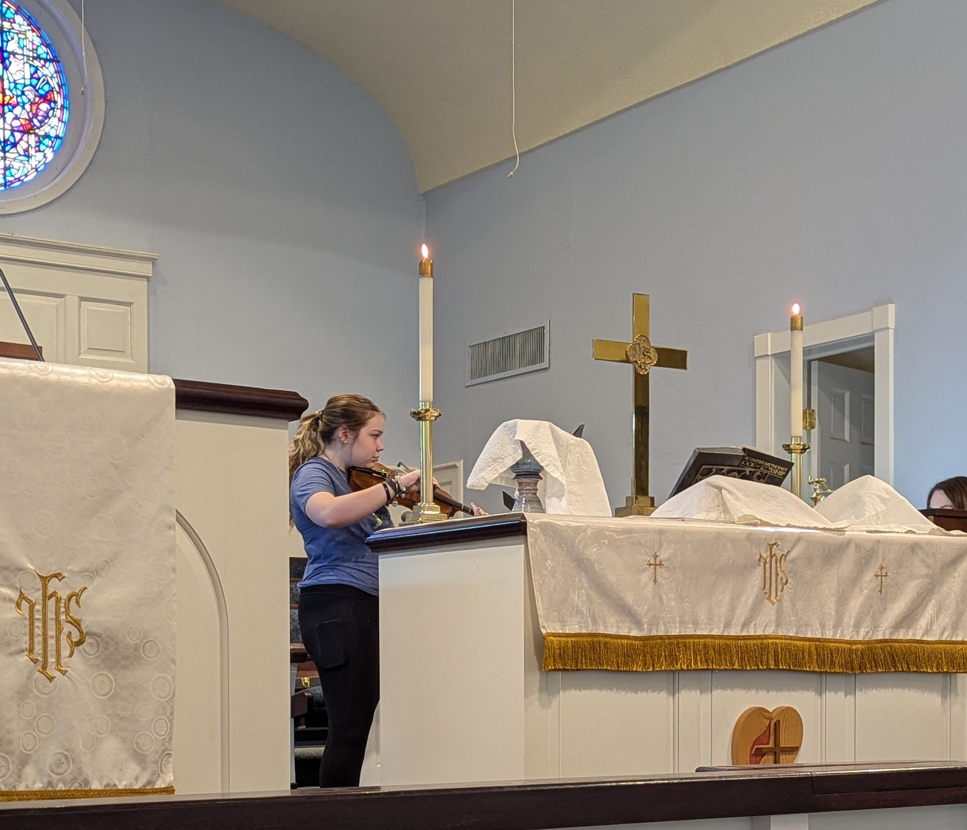 A young person plays a violin in a church, in front of the altar.
