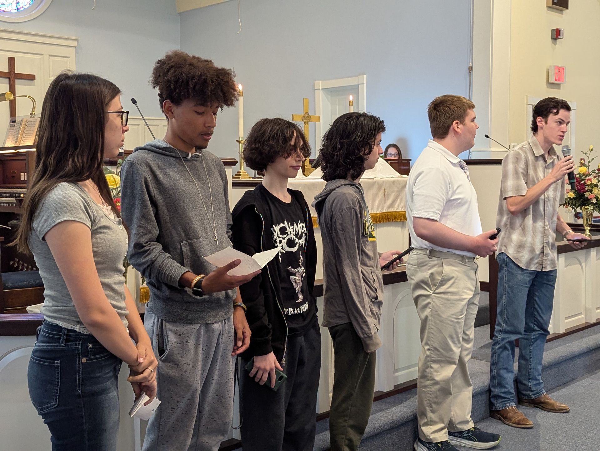 A group of teens standing at a church altar; one speaks into a microphone.