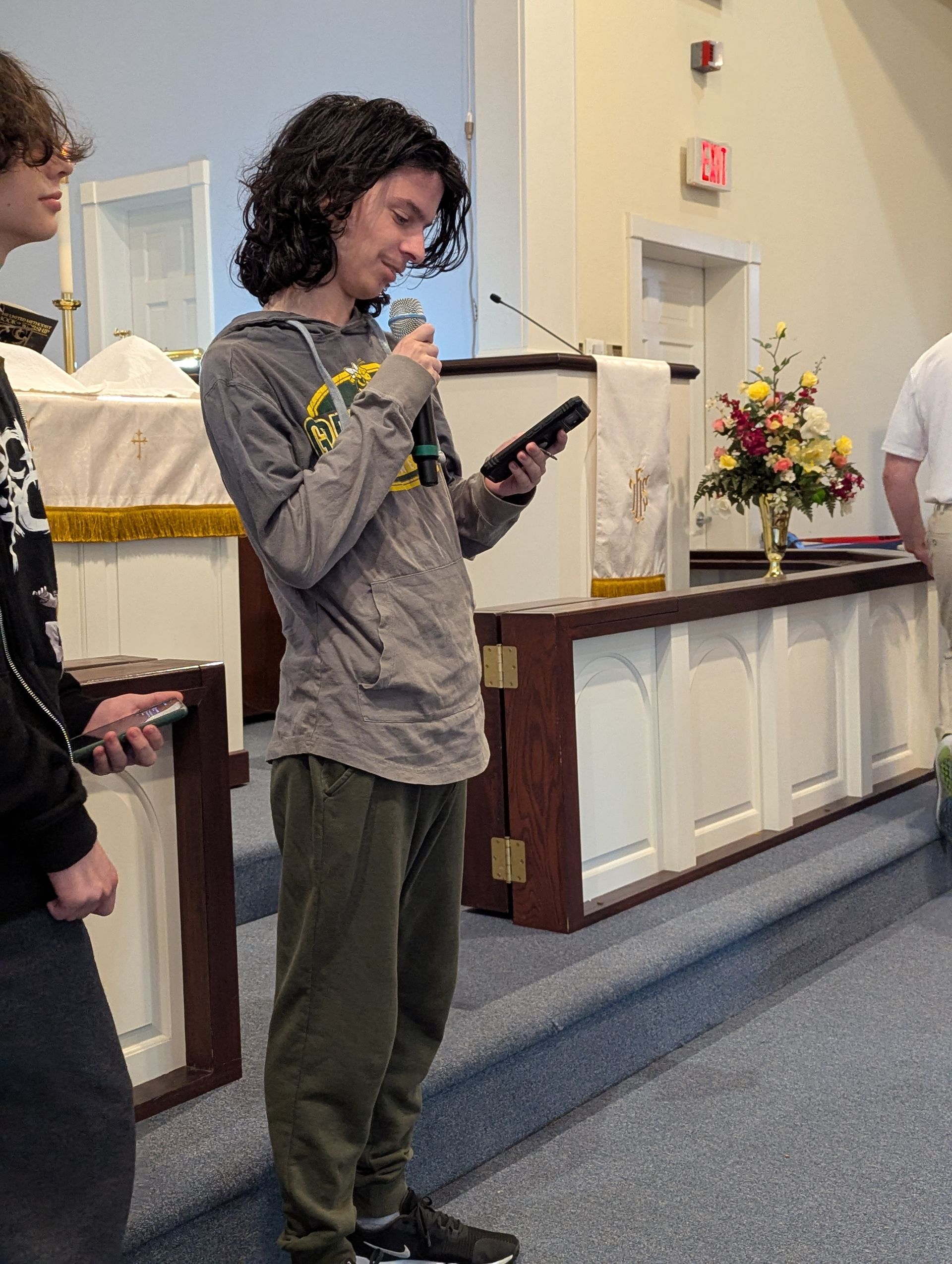 A young man with curly hair speaks into a microphone in a church.