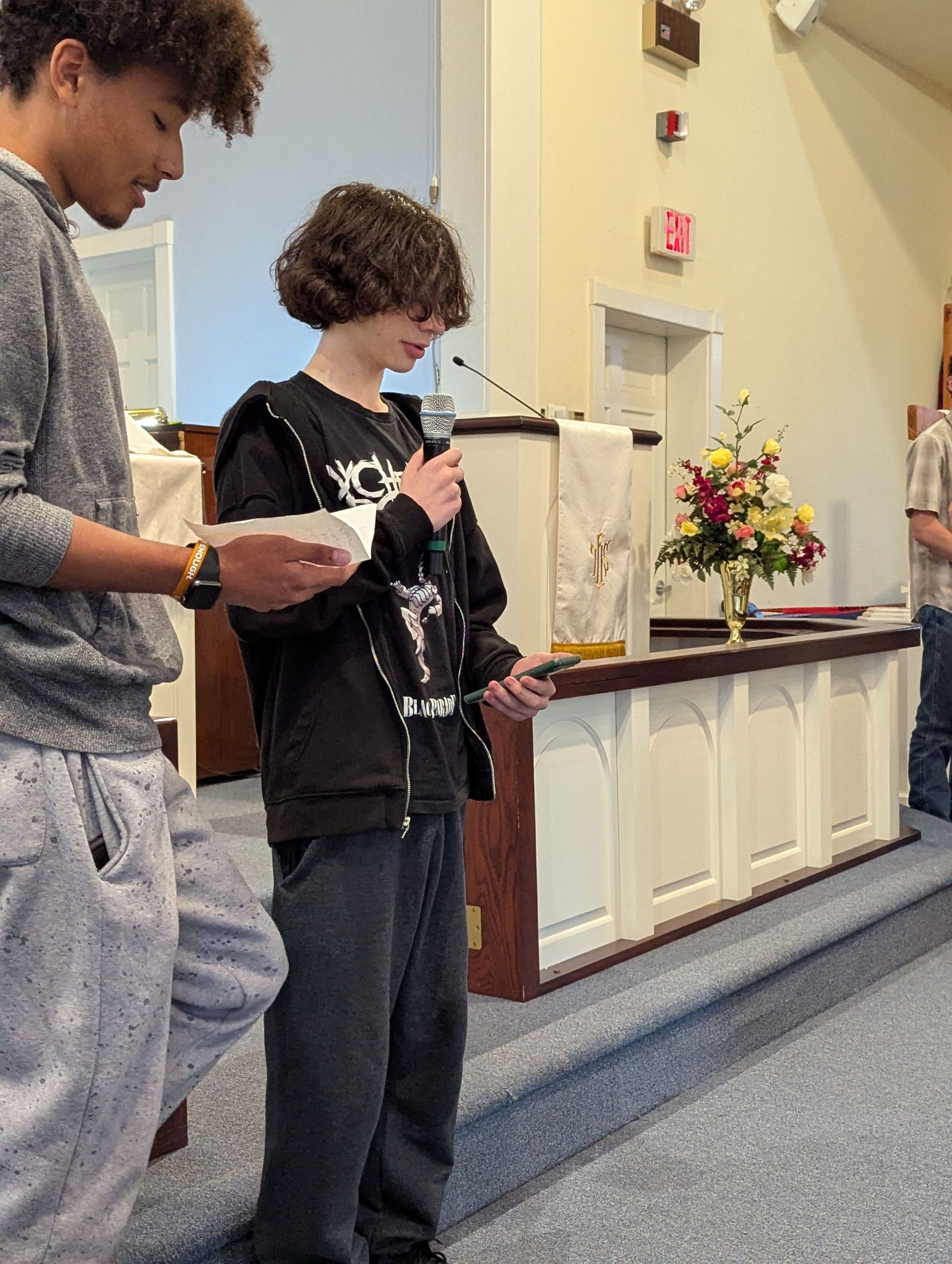 Two young people reading at a podium in a church. Boy with microphone, other boy reads alongside.
