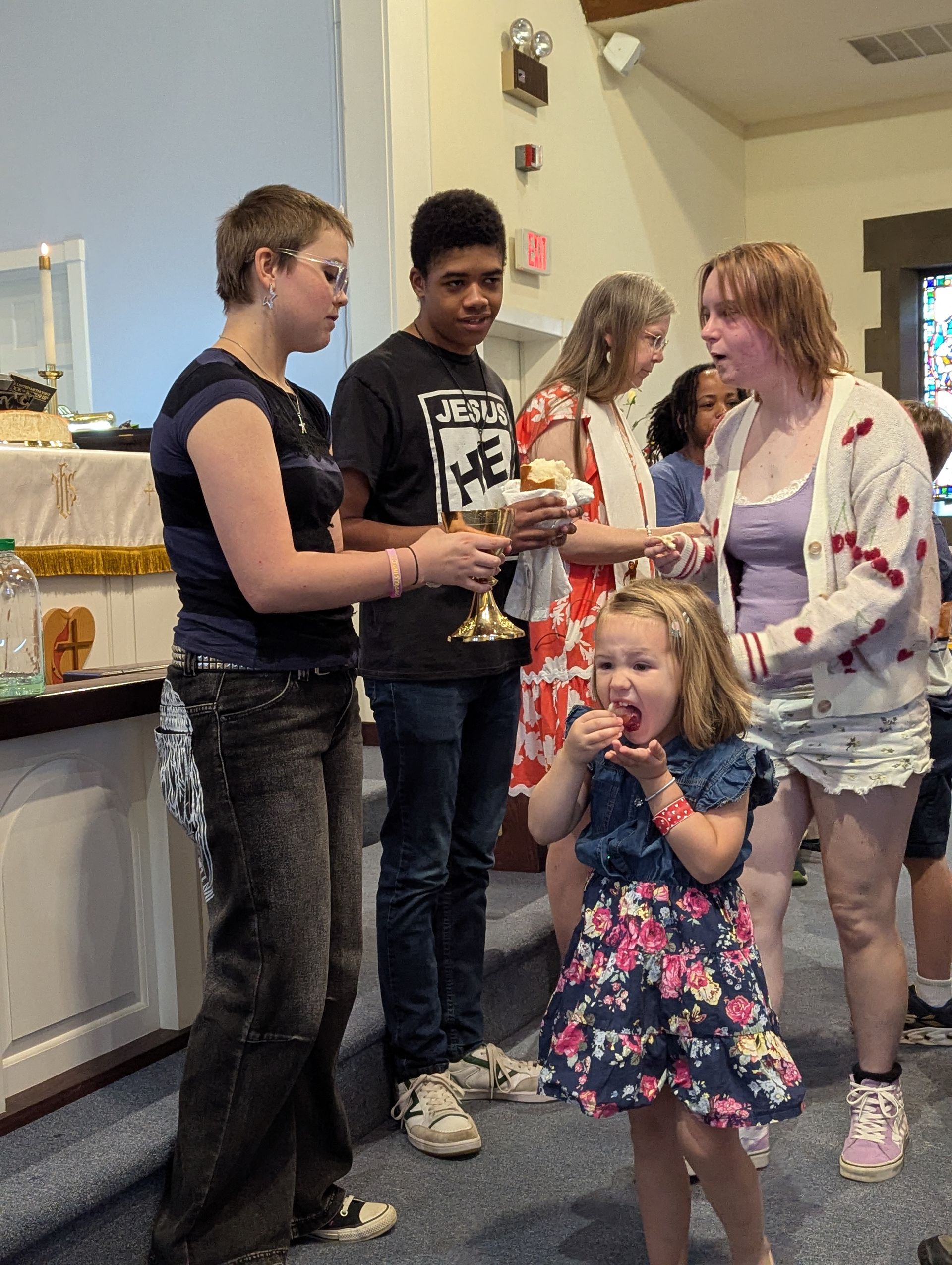 People in a church taking communion. A girl eats a wafer; others hold chalices, looking solemn.