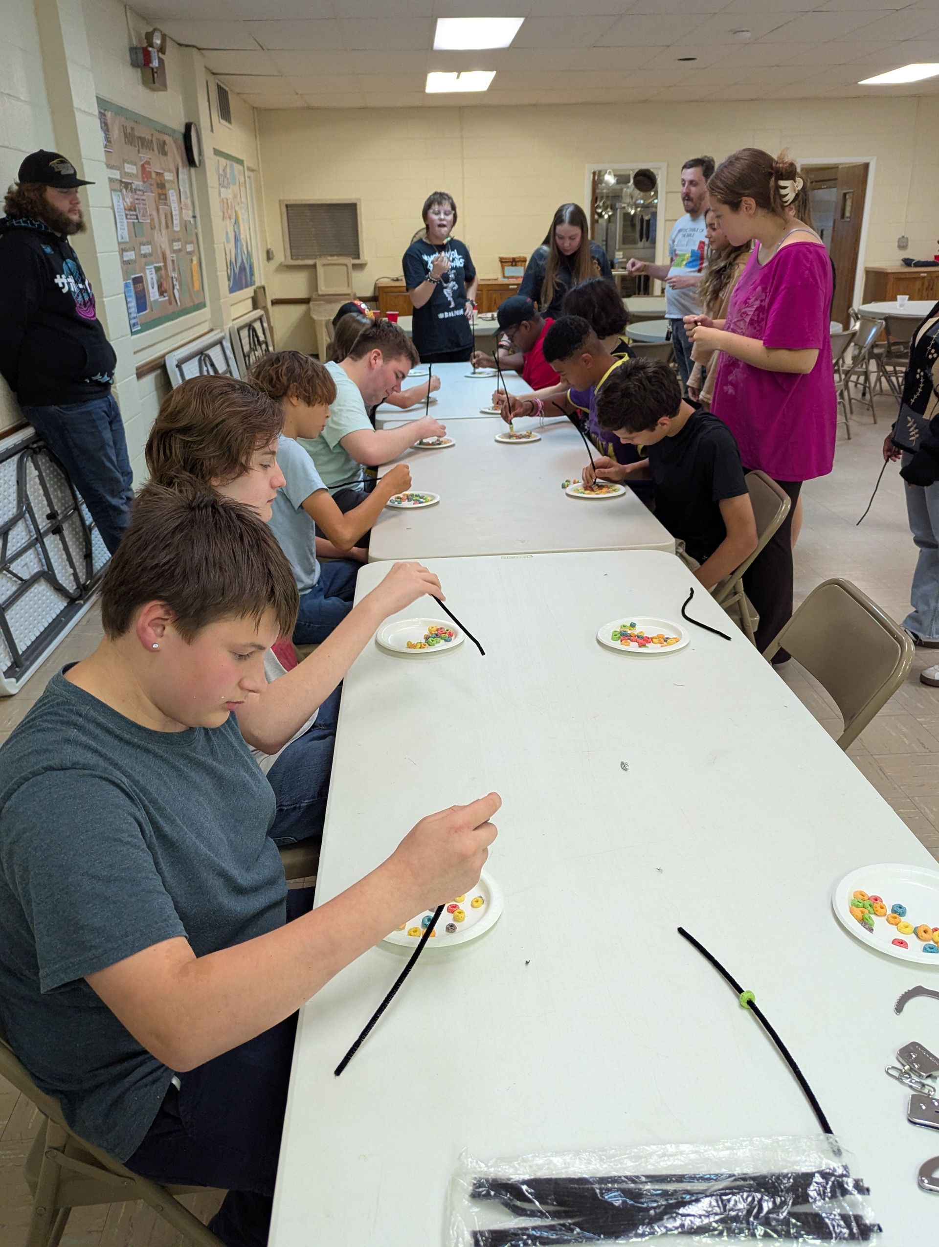 Youth seated at a table using chopsticks to pick up candy. A room setting.