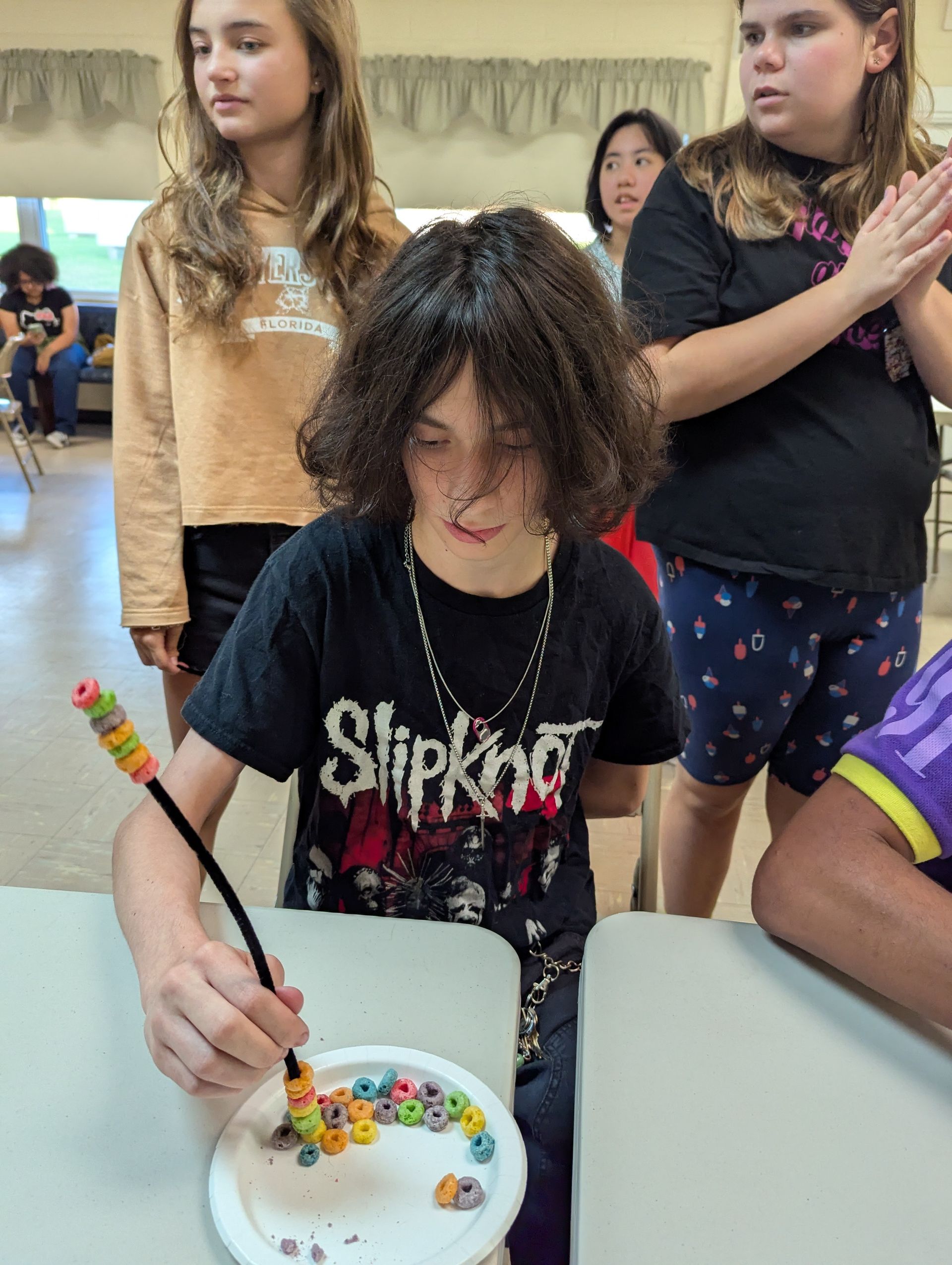 Youth crafting with cereal and pipe cleaner, surrounded by peers.