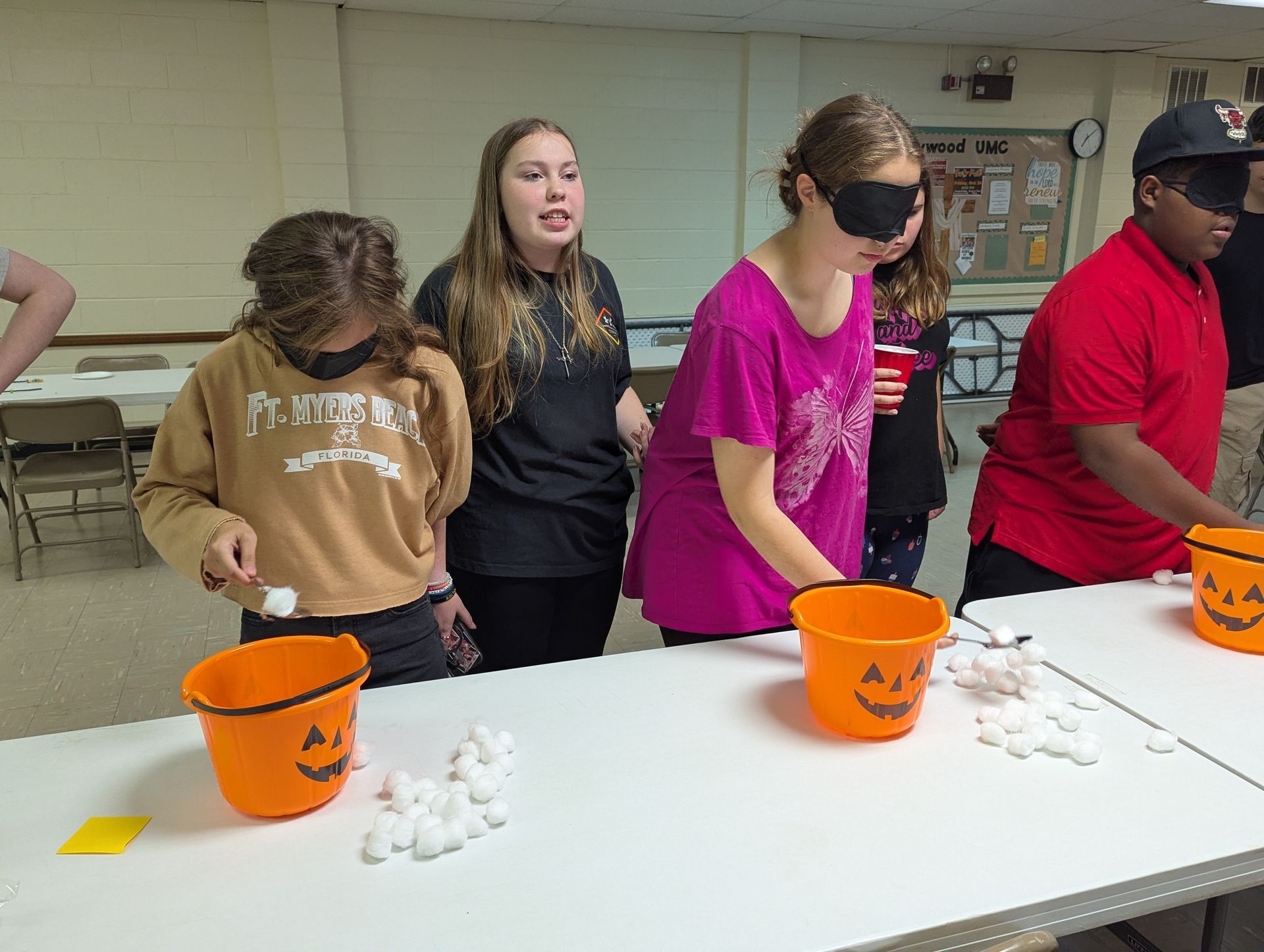 People playing a game with blindfolds, trying to toss cotton balls into pumpkin buckets.