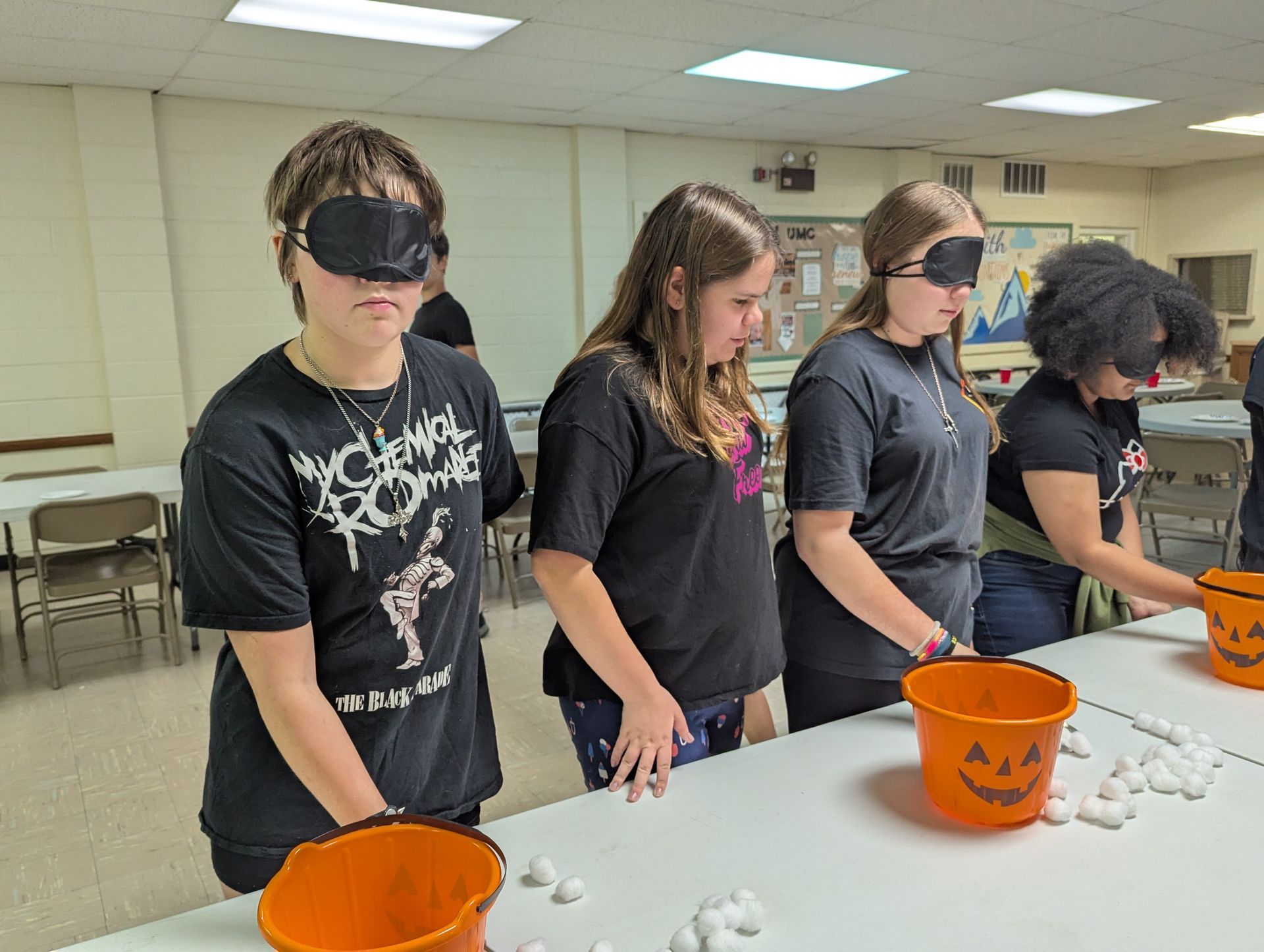 Four blindfolded people at a table, trying to put cotton balls in jack-o'-lantern buckets.
