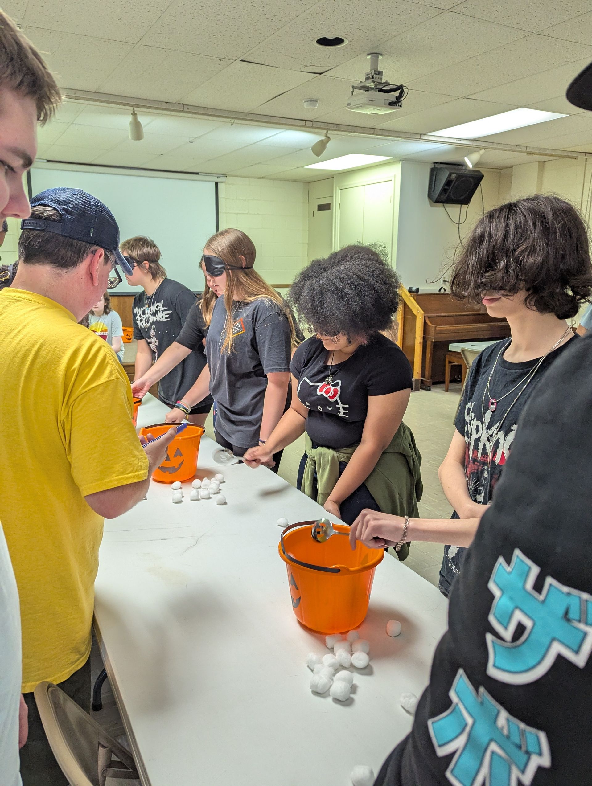 Youth playing a game, blindfolded, trying to toss cotton balls into orange buckets.