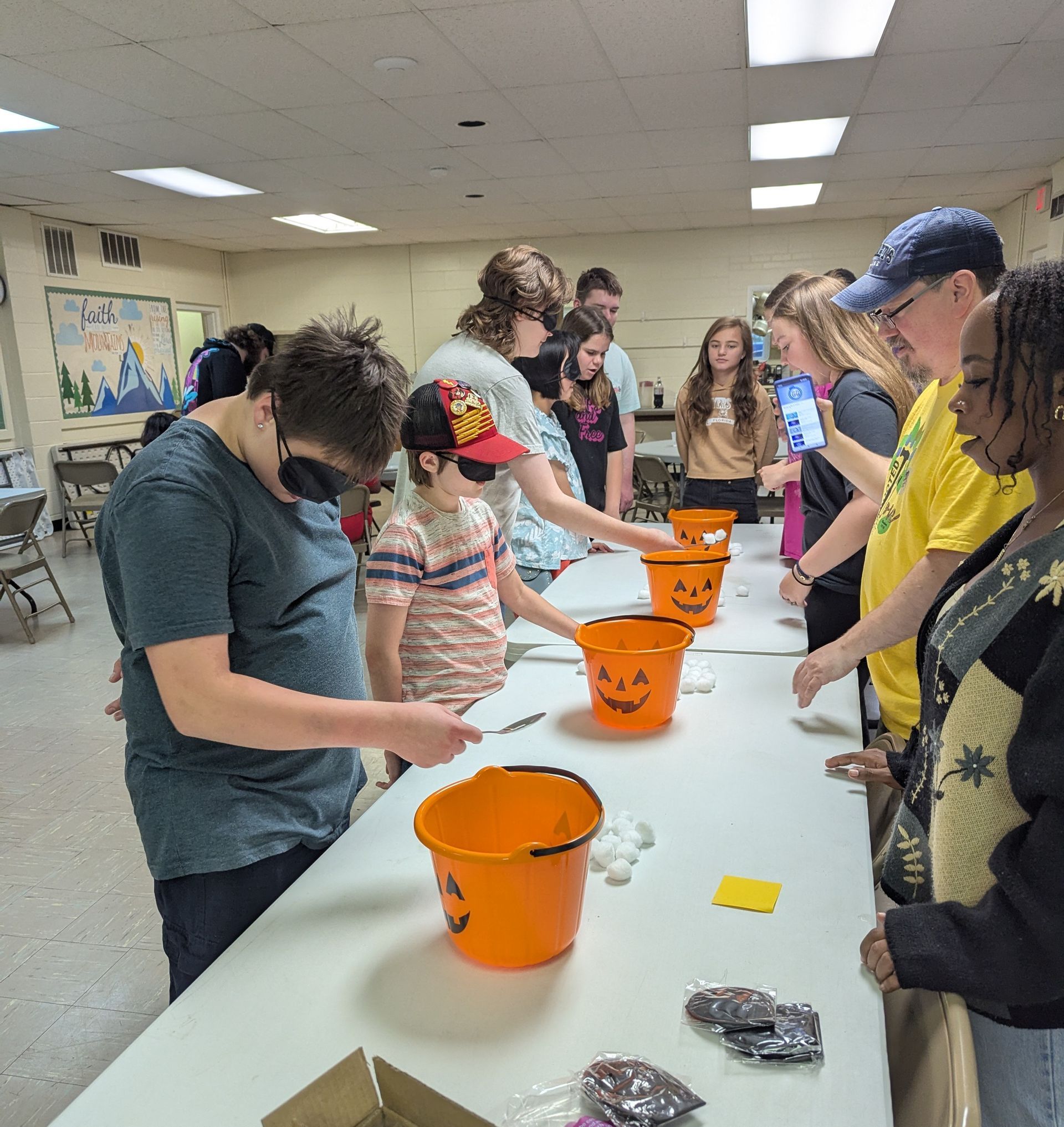 Group of teens at a table playing a Halloween-themed game. Blindfolded youth reach into buckets.