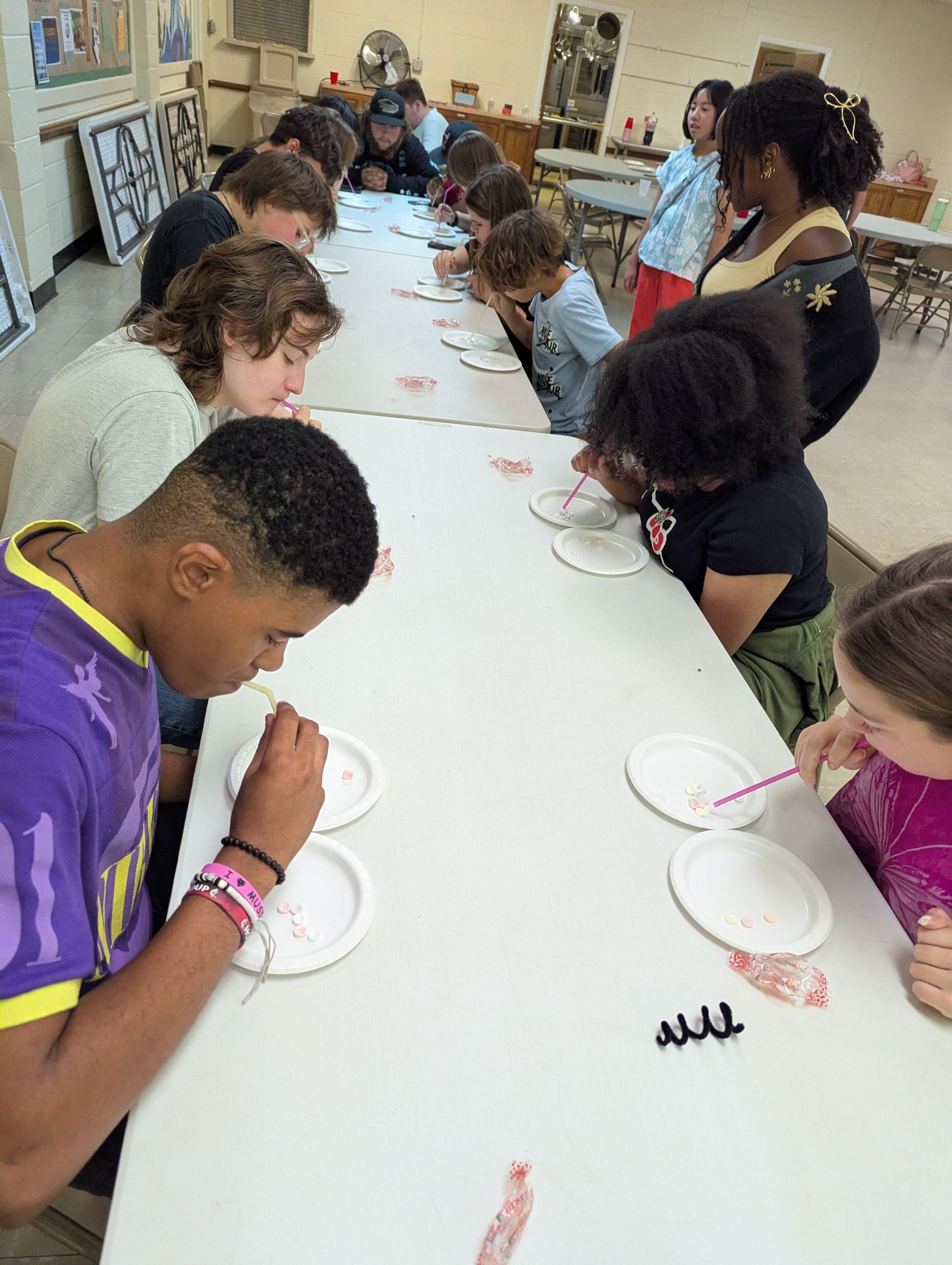 Group of youth blowing through straws at a long table in Galilee Hall
