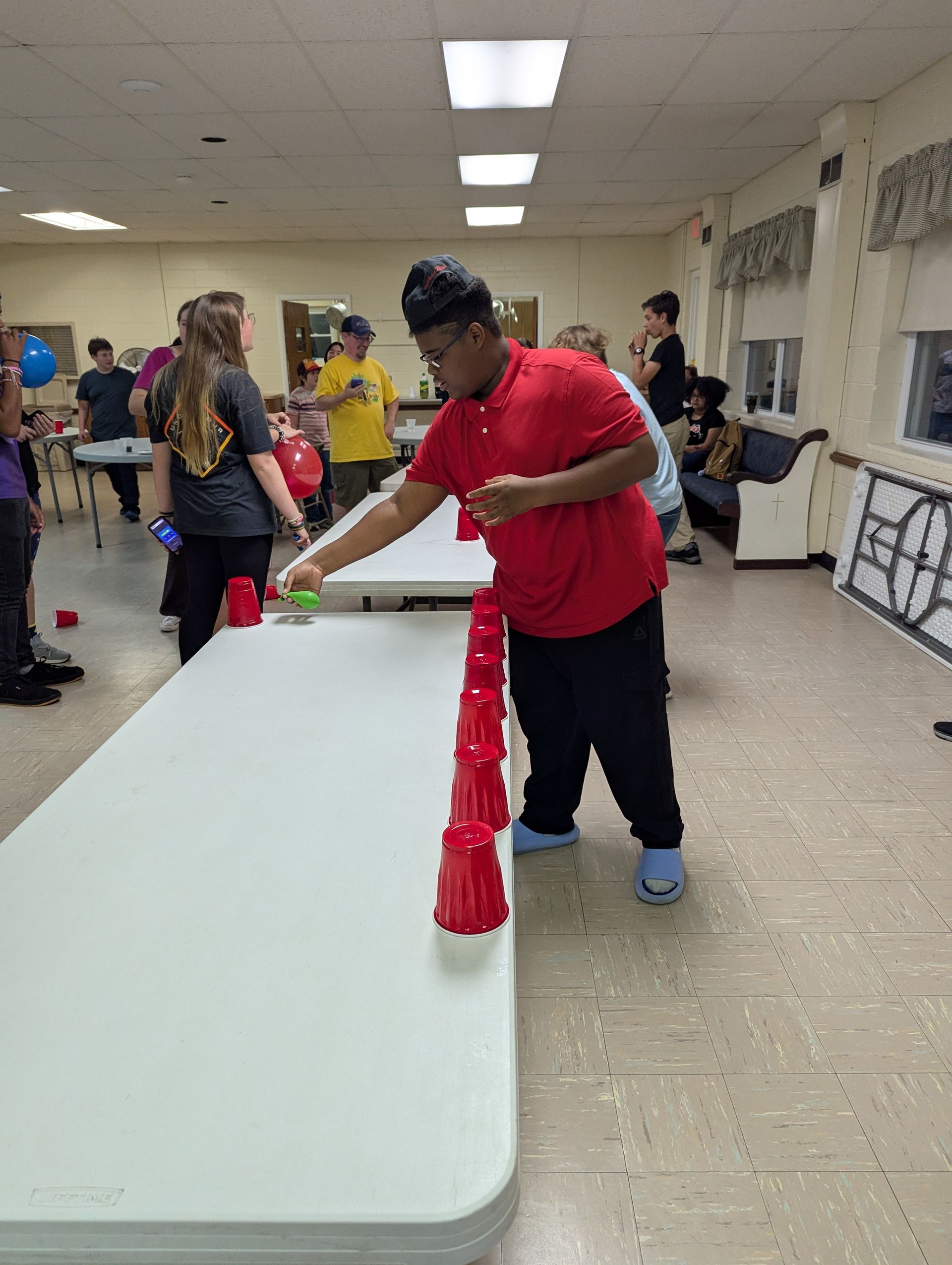 Youth stacking cups on a table at the 2025 Youth Group Kick off. Others watch.