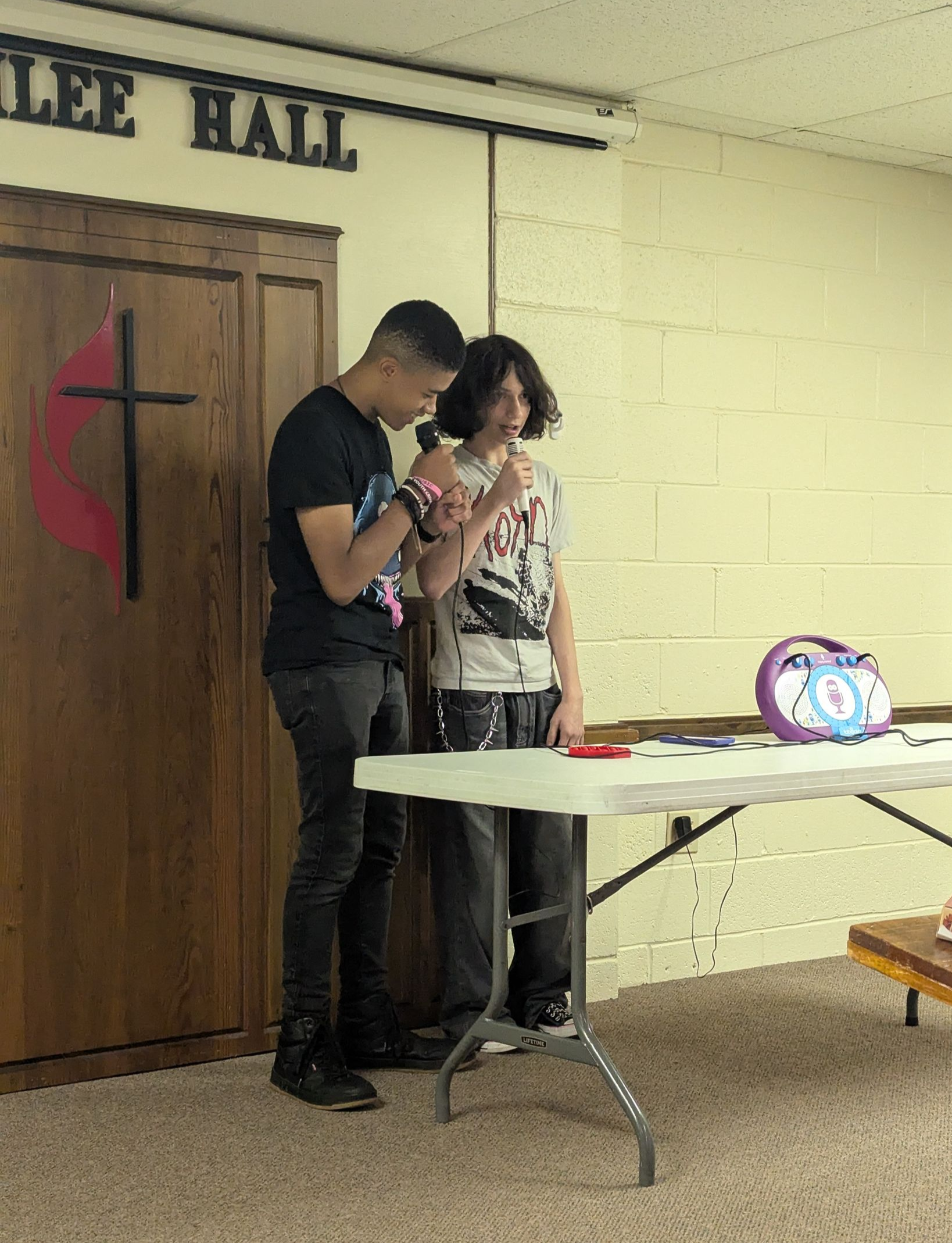 Two teens standing by a table in a hall.