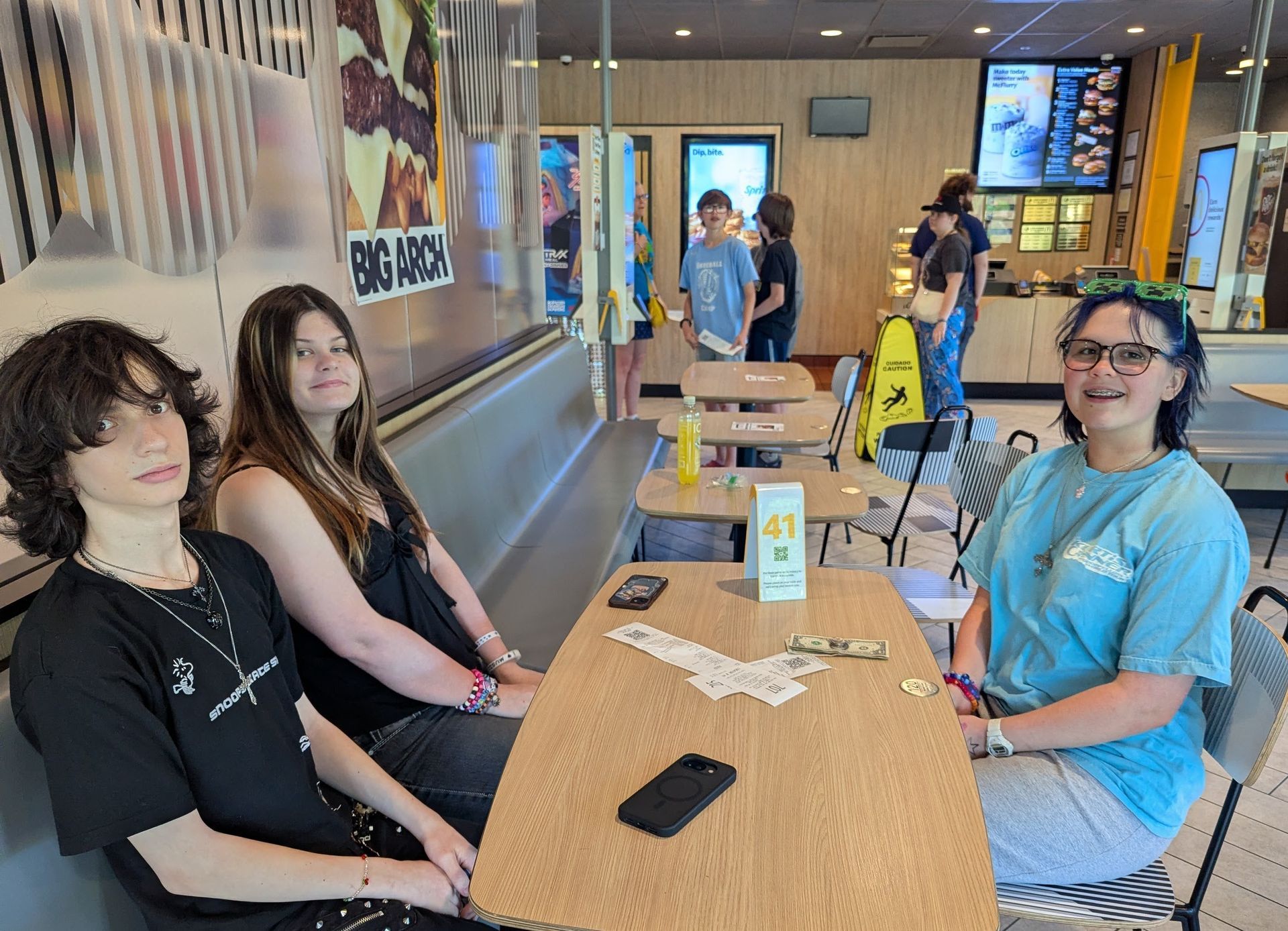 People seated at a long café table in a bright indoor lounge, one smiling at the camera.