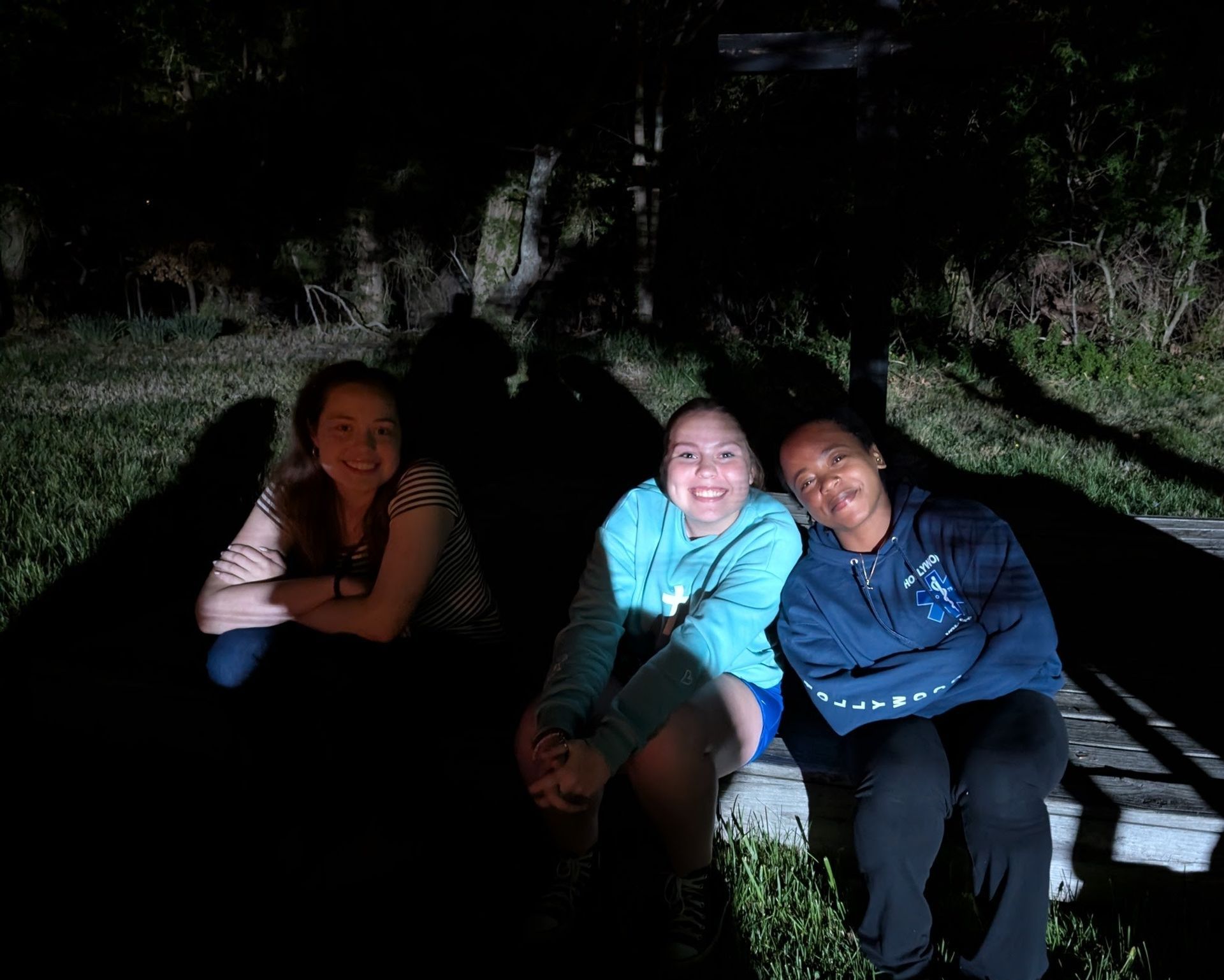 Three friends sitting on grass at night, around a campfire.