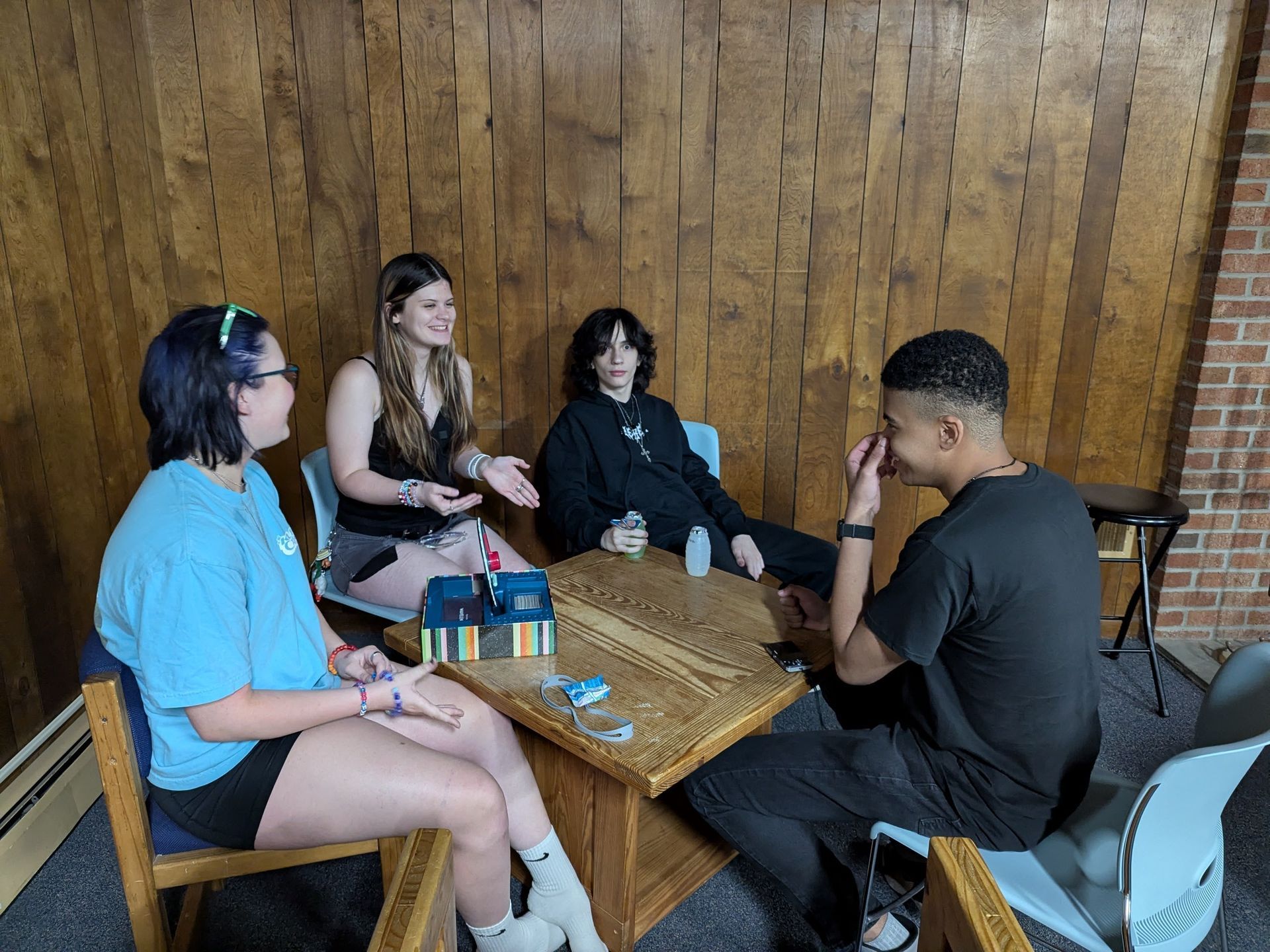 Youth sit around a low table in a wood-paneled lounge, chatting over a game.