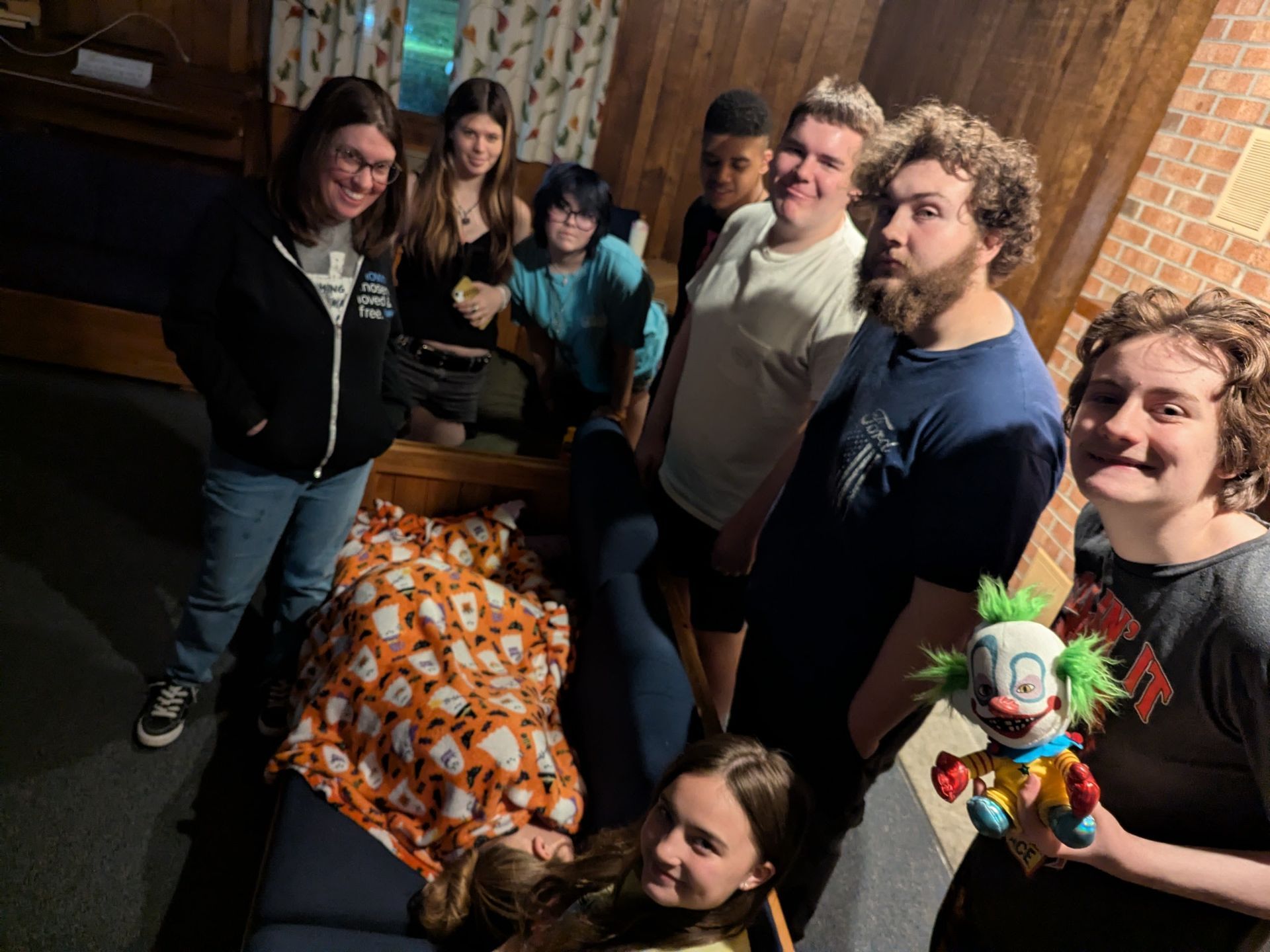 Group of people gathered indoors around a table, with one person holding a colorful toy puppet.