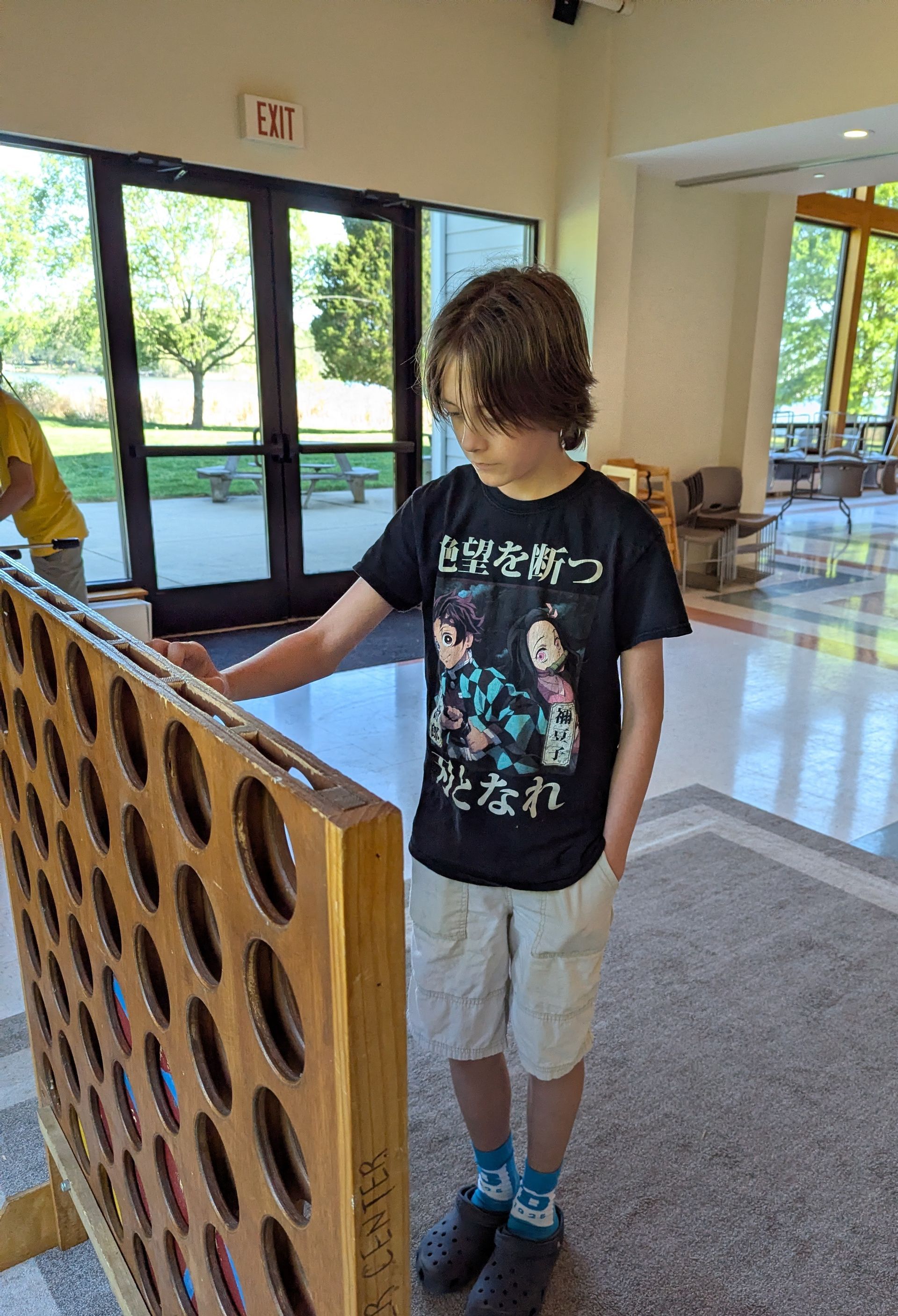 Person in a black graphic T-shirt stands beside a wooden panel in a bright indoor lobby.