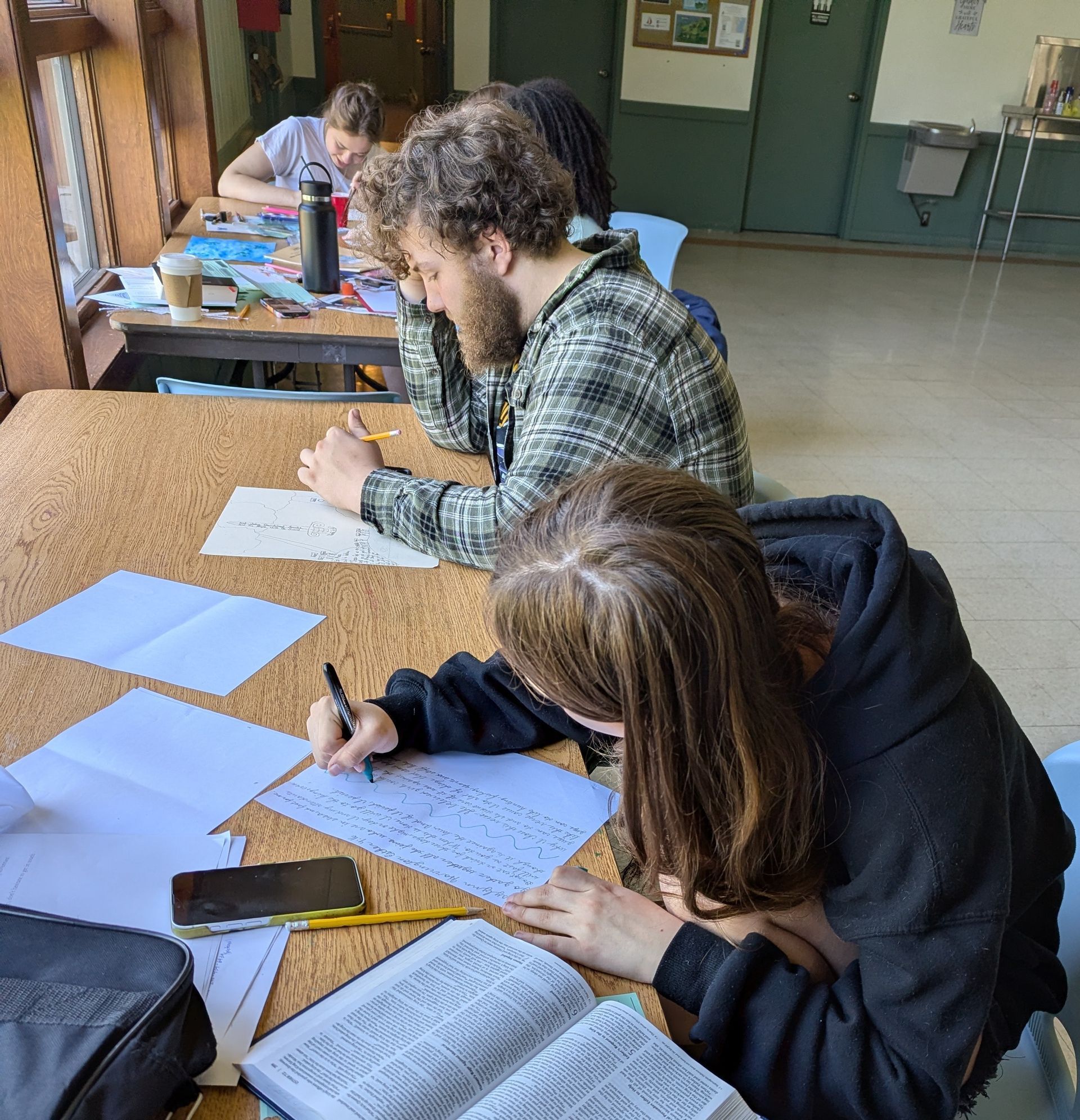 Youth writing on papers at a table in a classroom or workshop setting