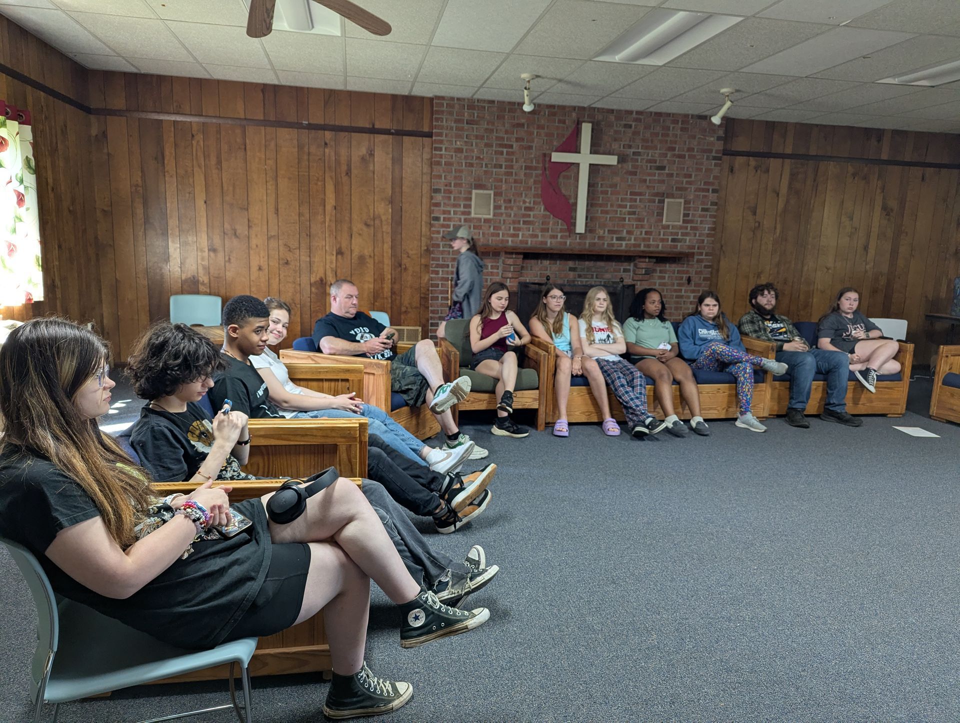 Youth seated in a wood-paneled room with a cross on the wall, listening in a small meeting.