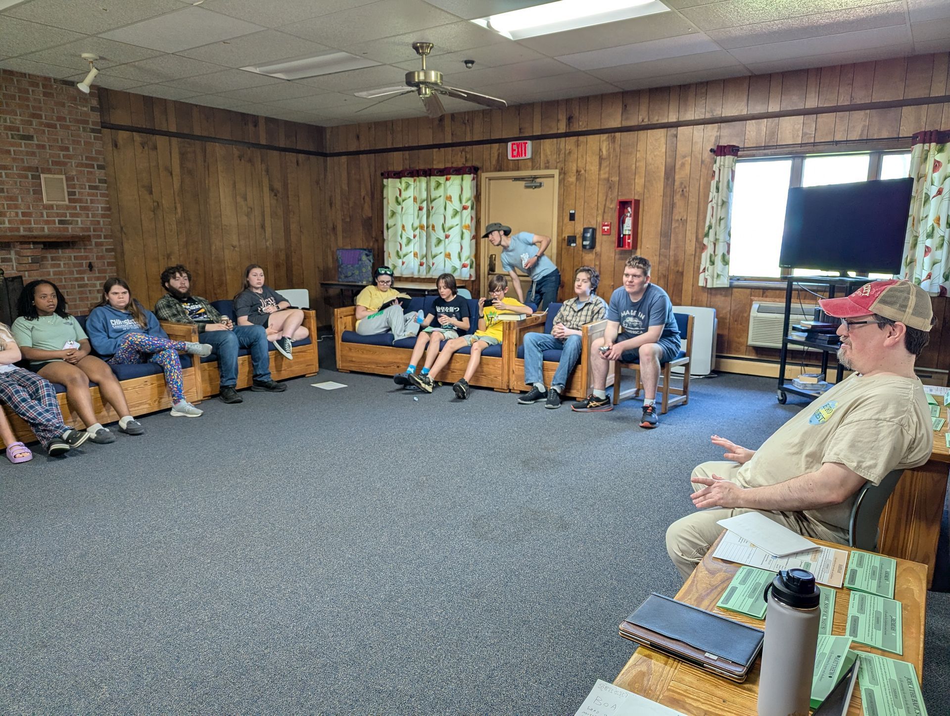 Youth seated in a community room with wood-paneled walls and a carpeted floor, facing a discussion.