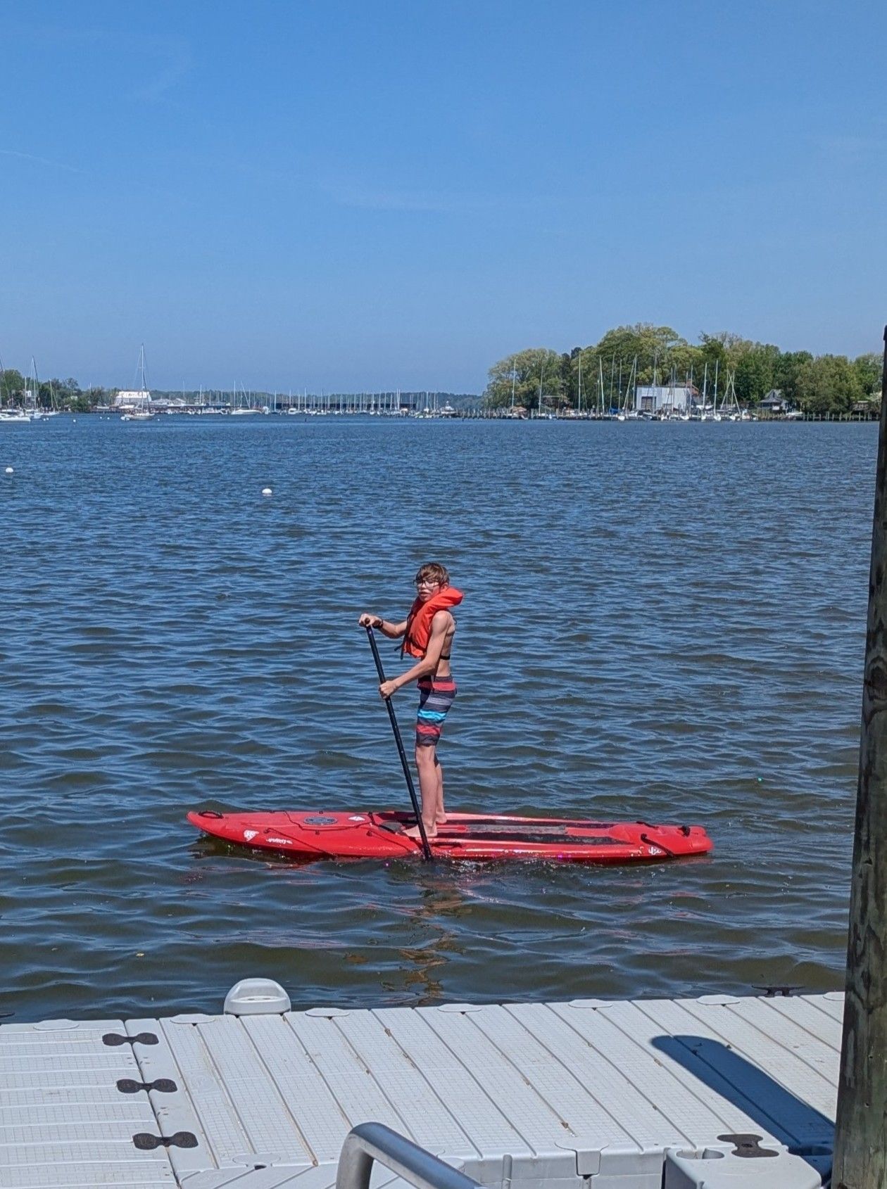 Person in red on a paddleboard on a lake near a dock under a clear blue sky.