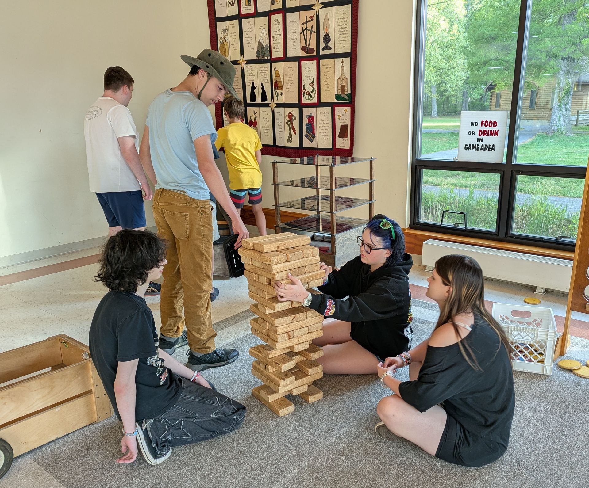 People playing giant Jenga indoors near large windows and framed artwork.