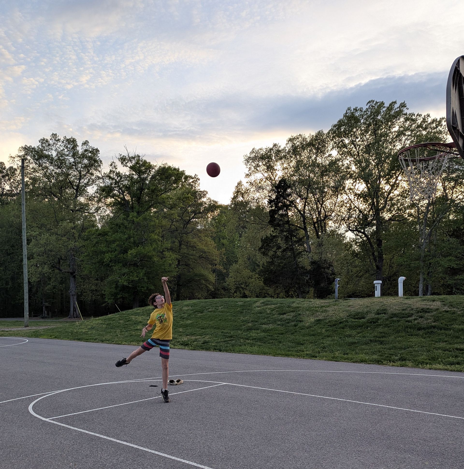 A youth in yellow shirt kicking a ball on an outdoor court at dusk