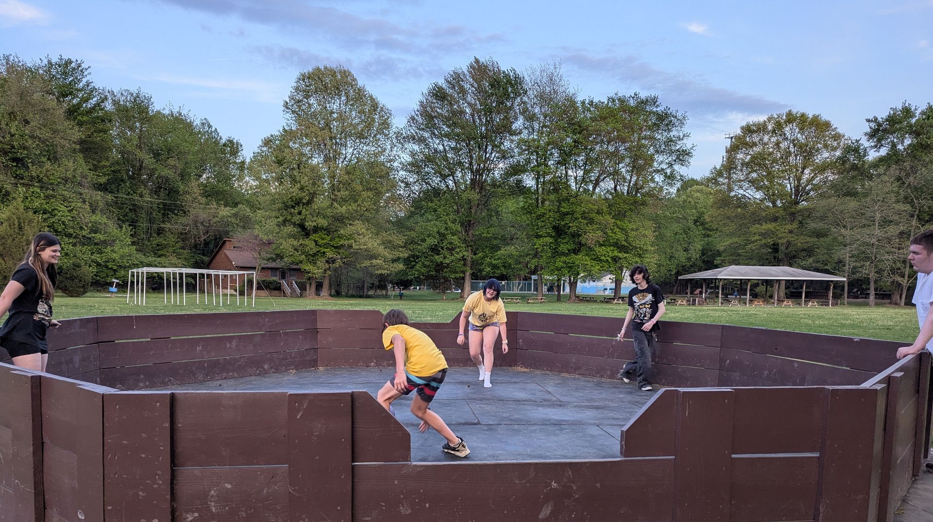 People playing in a fenced, brown-walled outdoor skatepark under a blue sky.