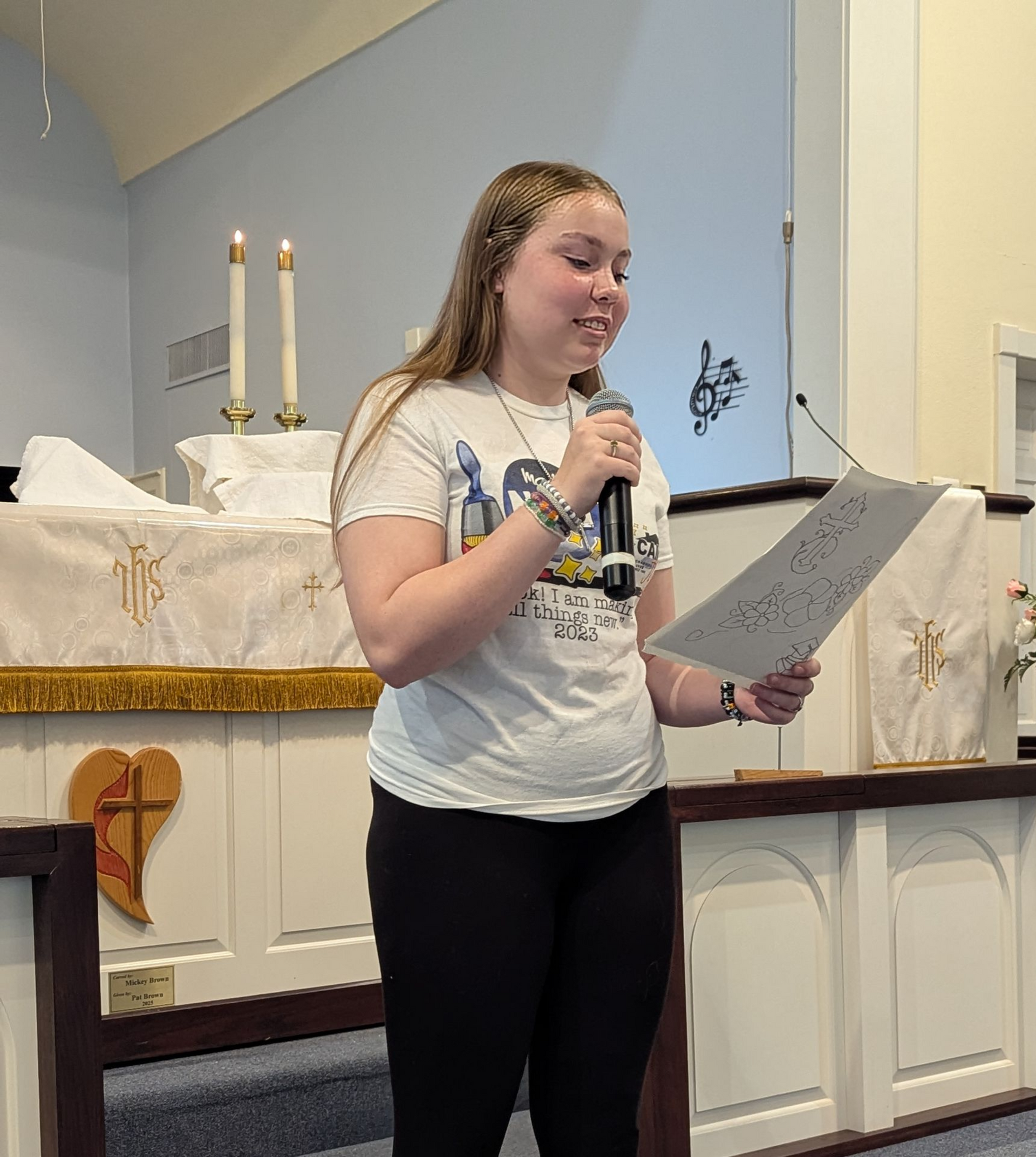 Teen speaking at a church altar while holding a microphone and notes.