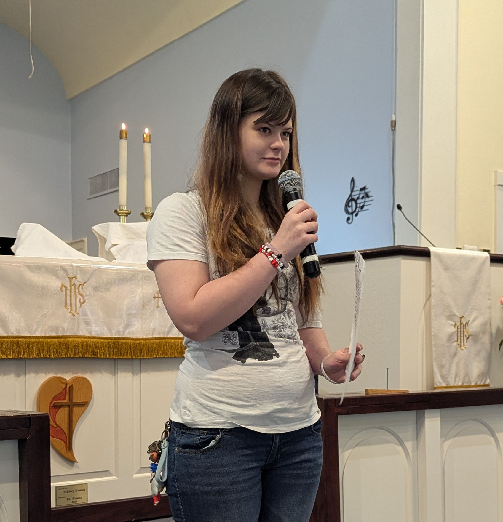 Youth speaking into a microphone at a church altar, with candles and white cloth decorations.