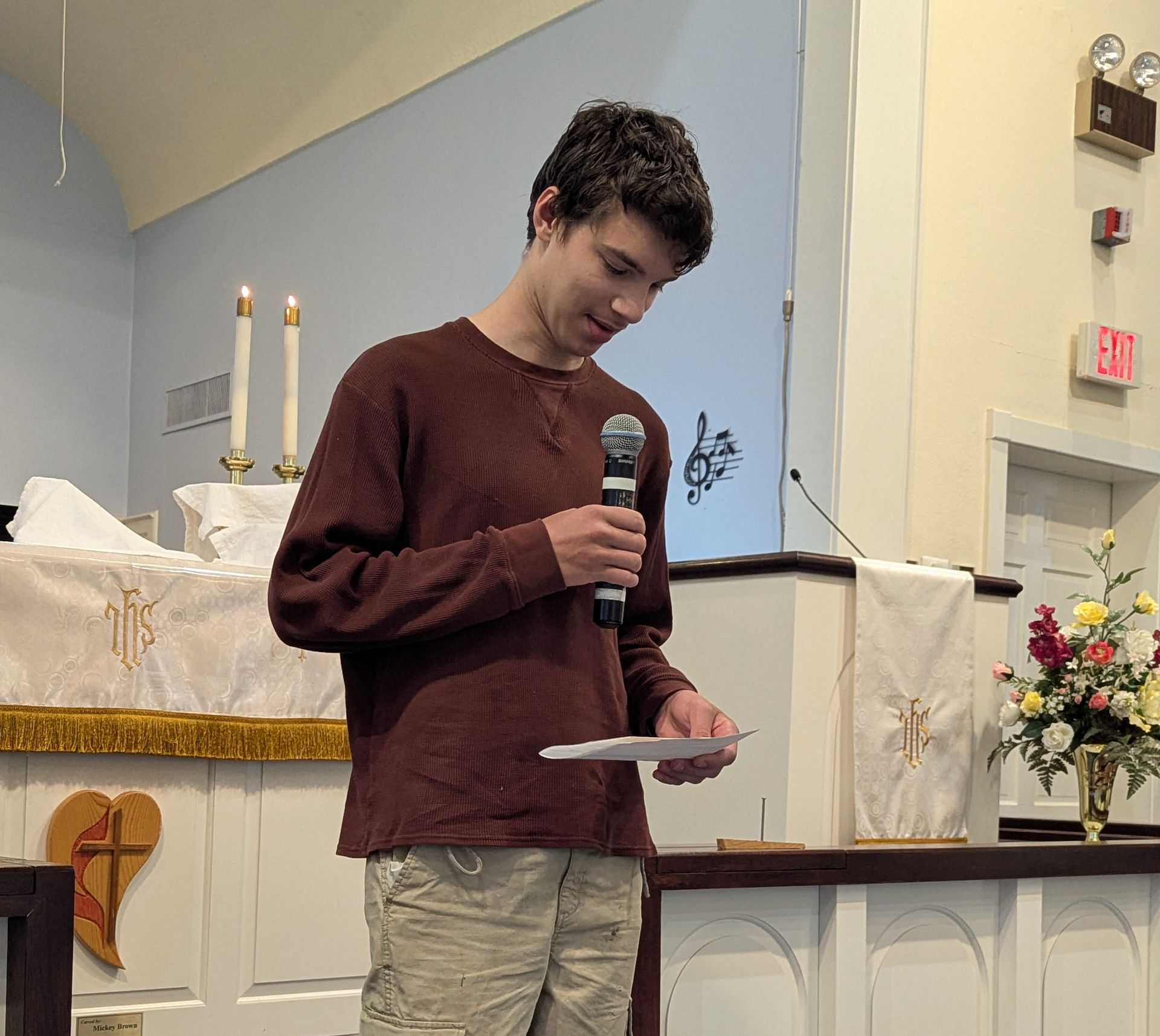 Youth speaking into a microphone at a church altar while reading from a sheet of paper