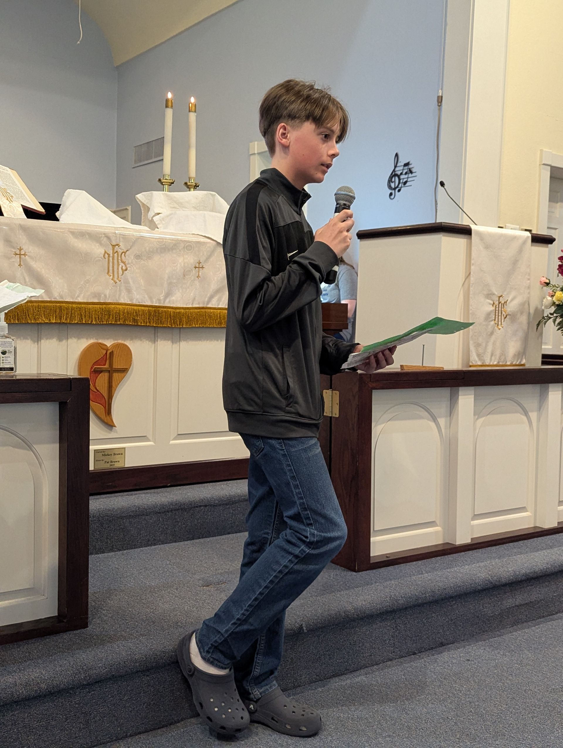 Youth walking on a church stage holding a microphone and notes beside the altar