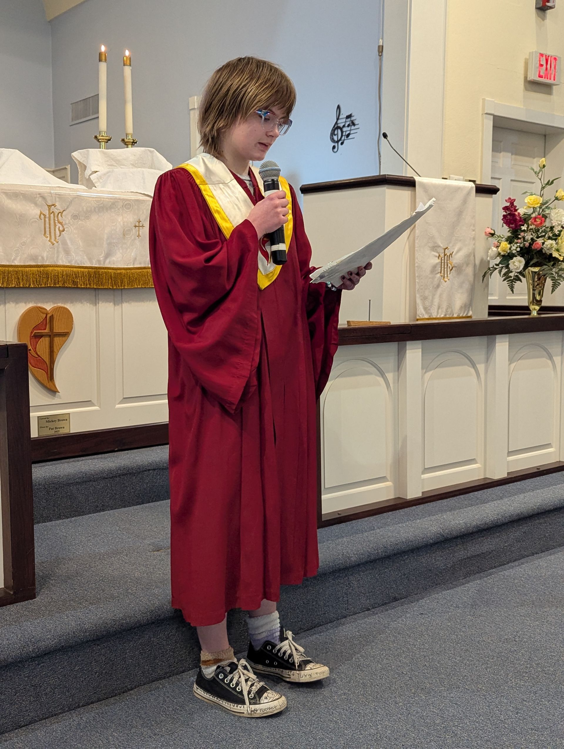 Youth in red robe reading at a church lectern beside the altar
