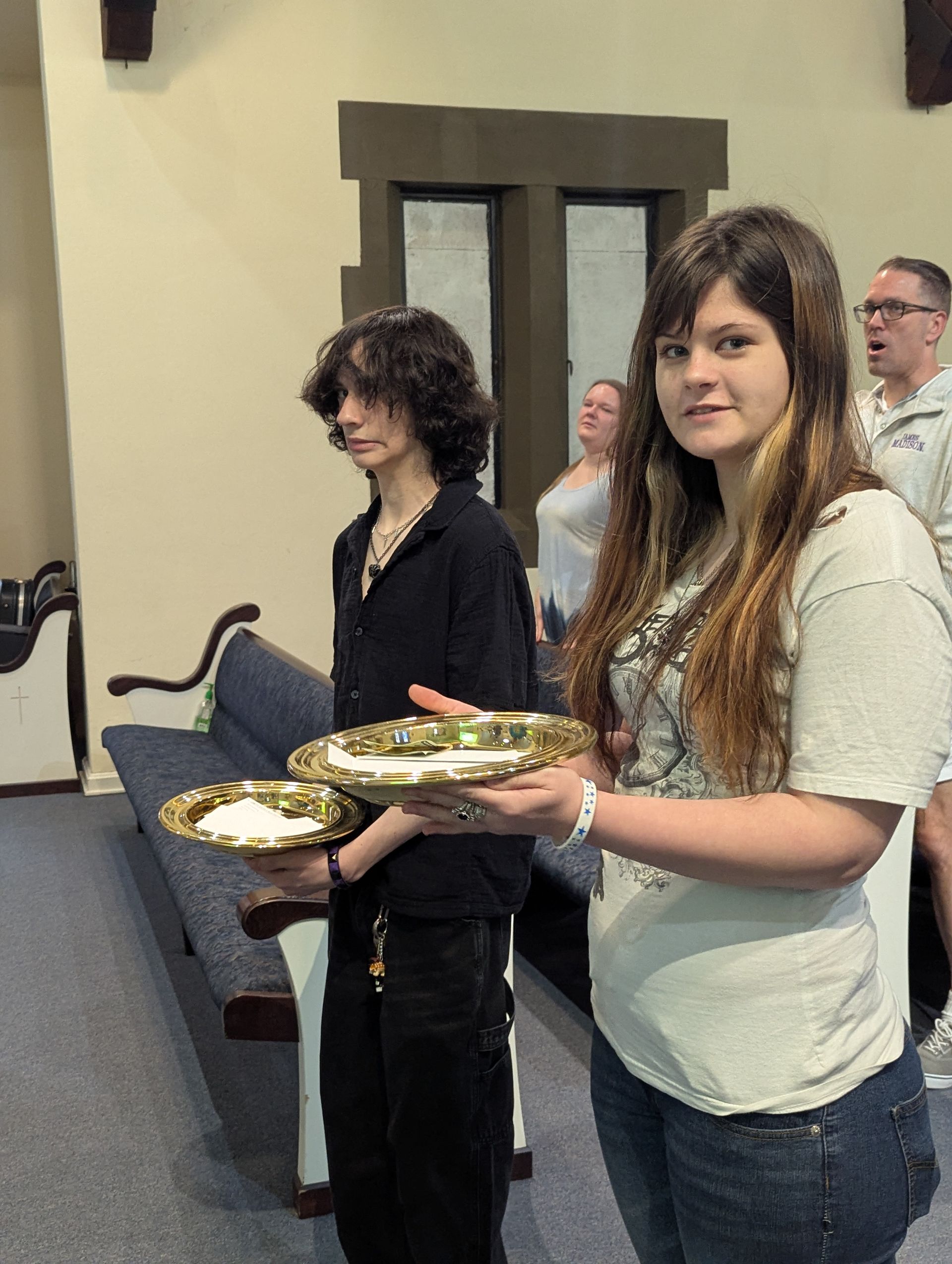 Two people hold offering plates in front of the alter with others standing in the background.