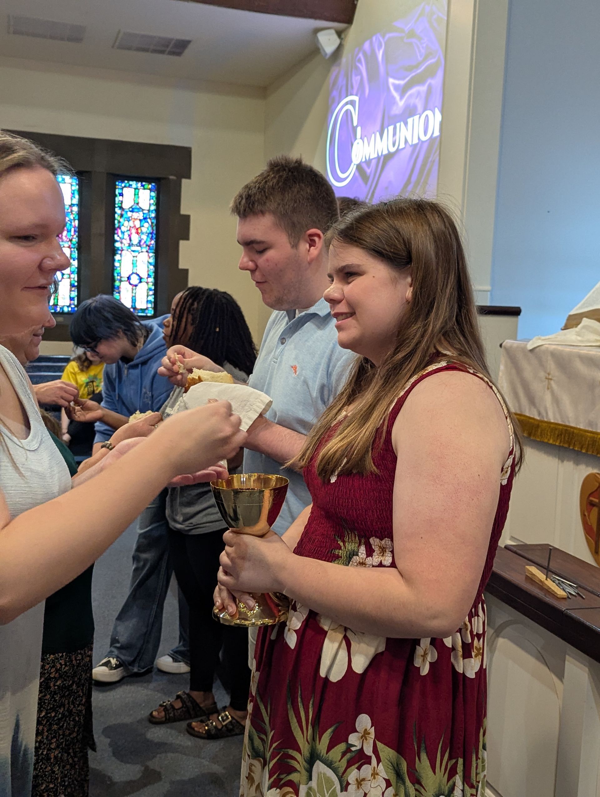Youth giving communion near a projected screen.