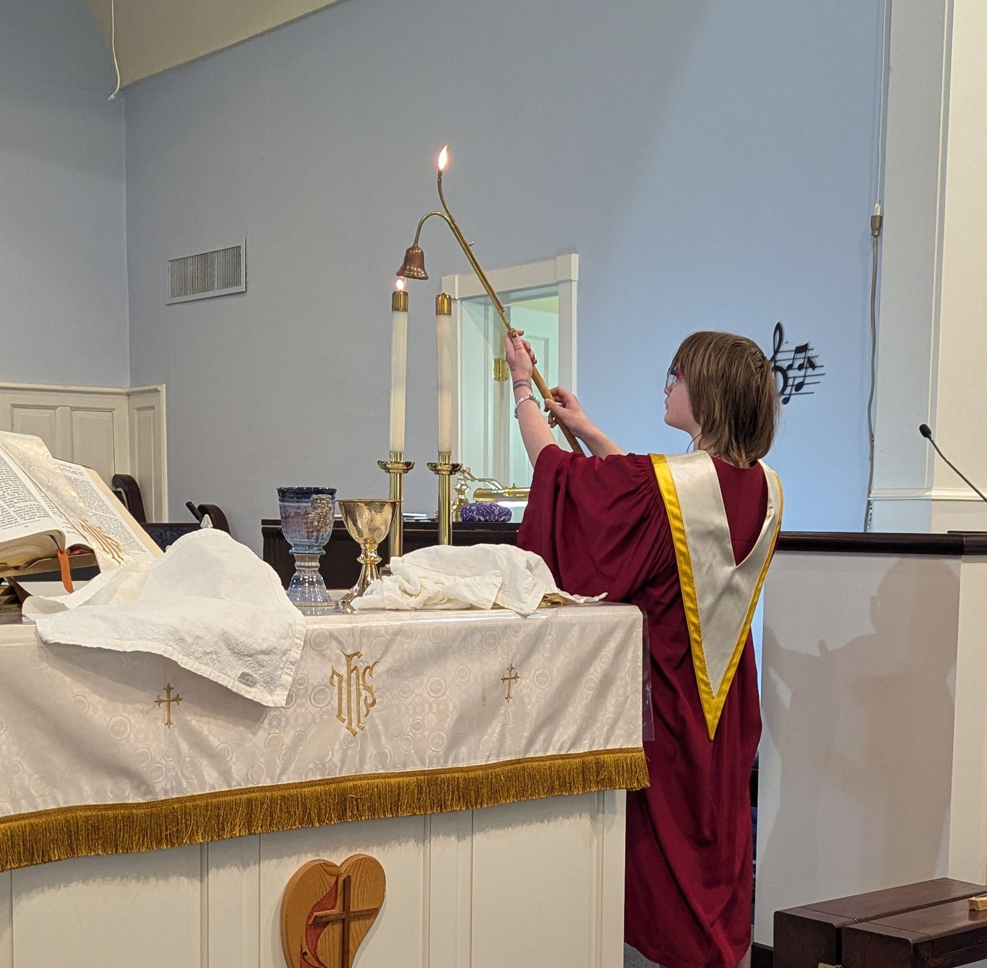Person in red robe lighting a candle at an altar in a church
