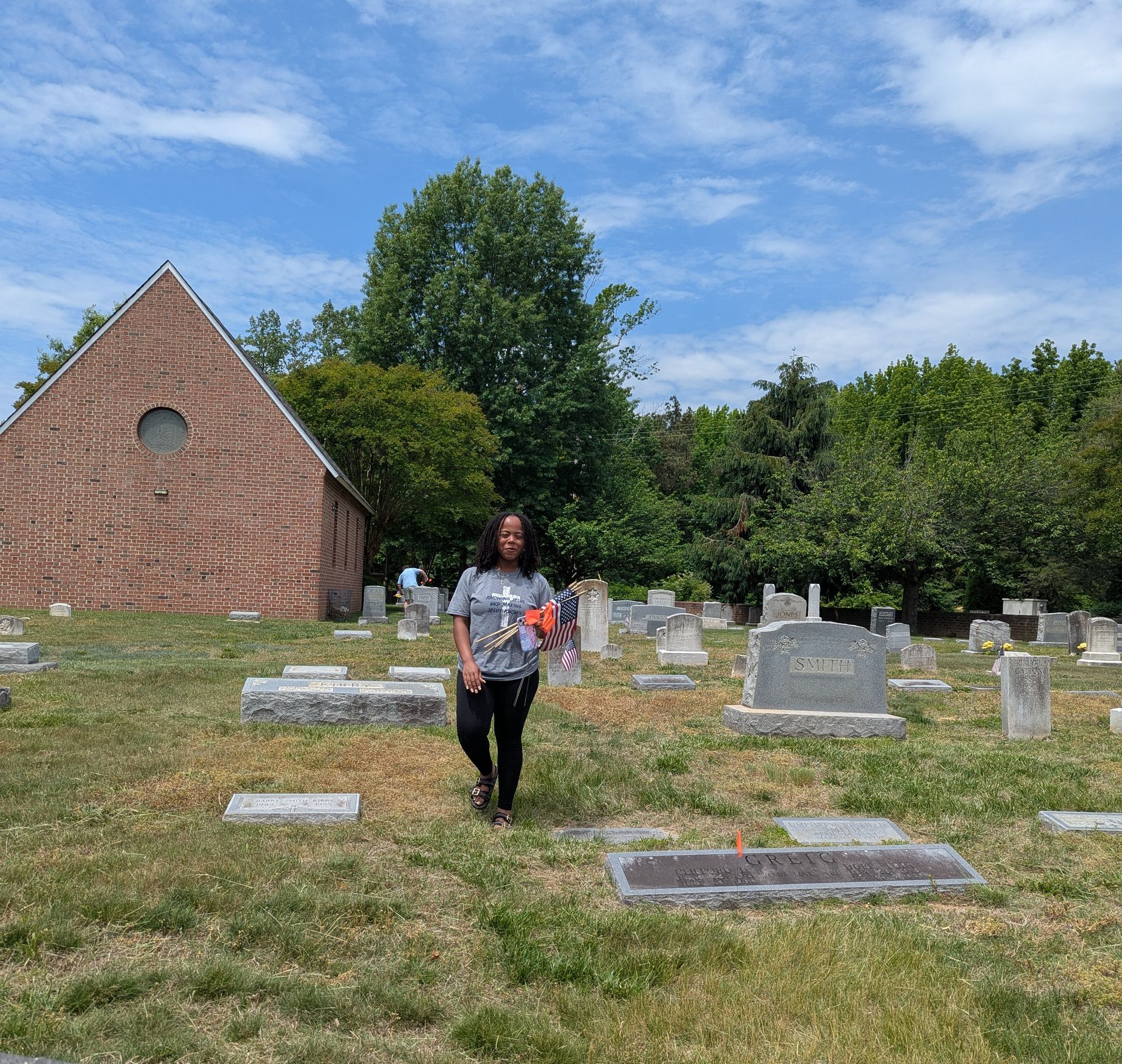 A youth walking through a cemetery beside a brick chapel on a sunny day