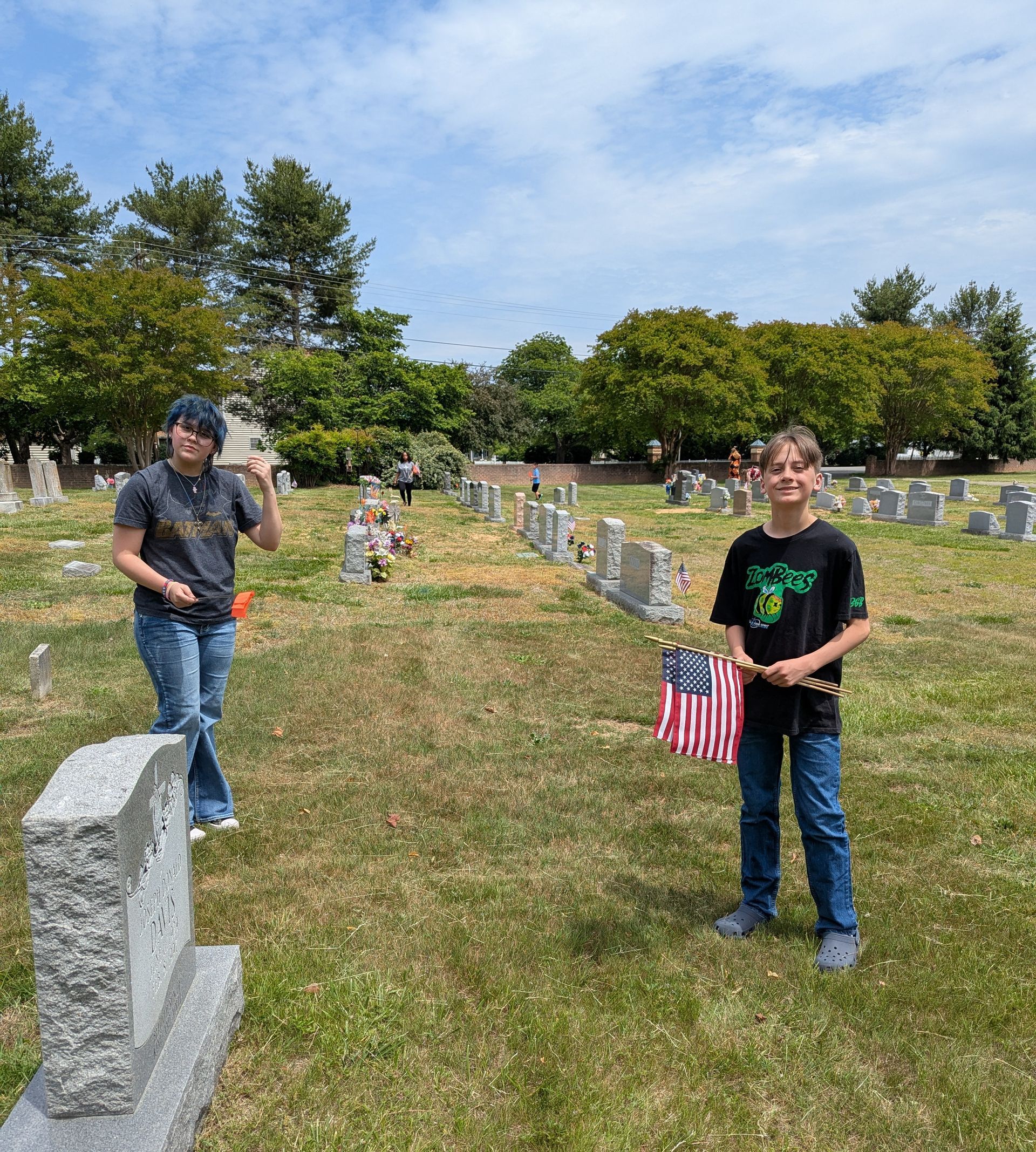 Two youth in a cemetery, one holding a small American flag on a sunny day