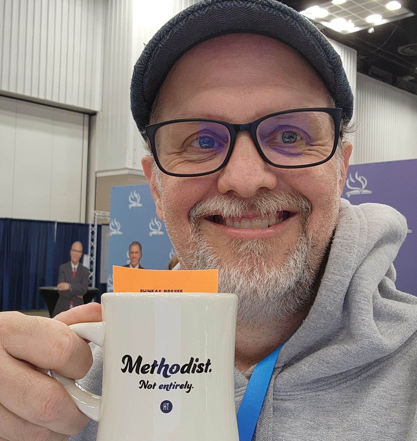 Man with glasses, beanie, and beard smiling, holding a 