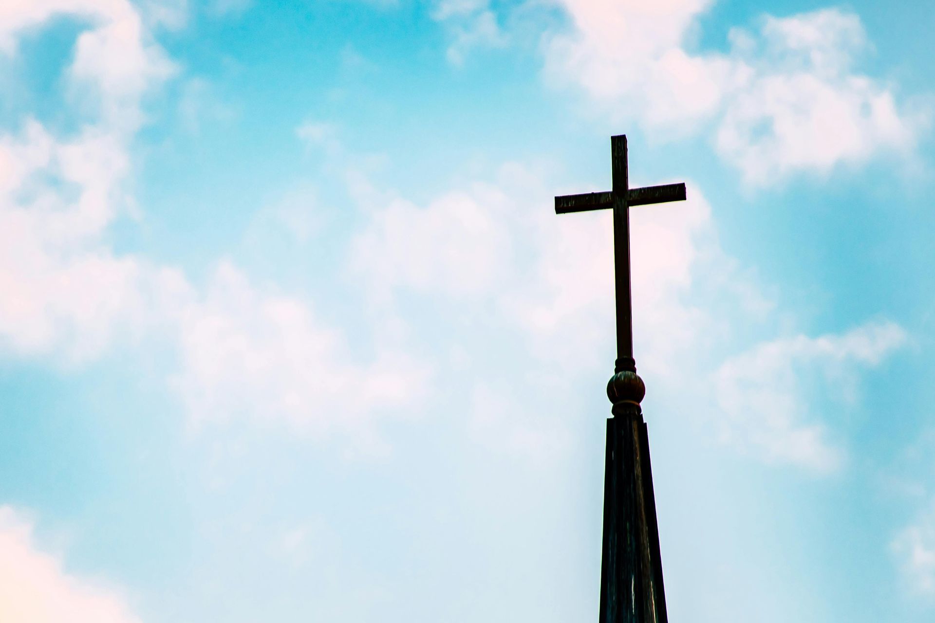 Cross silhouetted atop a church steeple against a blue sky with pink clouds