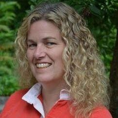 A woman with curly hair is wearing a red shirt and smiling.