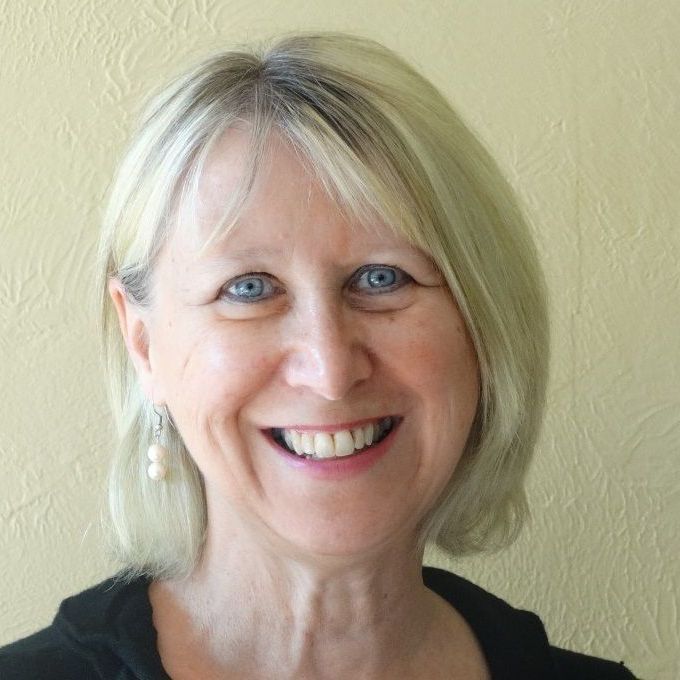 A woman with blonde hair and blue eyes is smiling for the camera.
