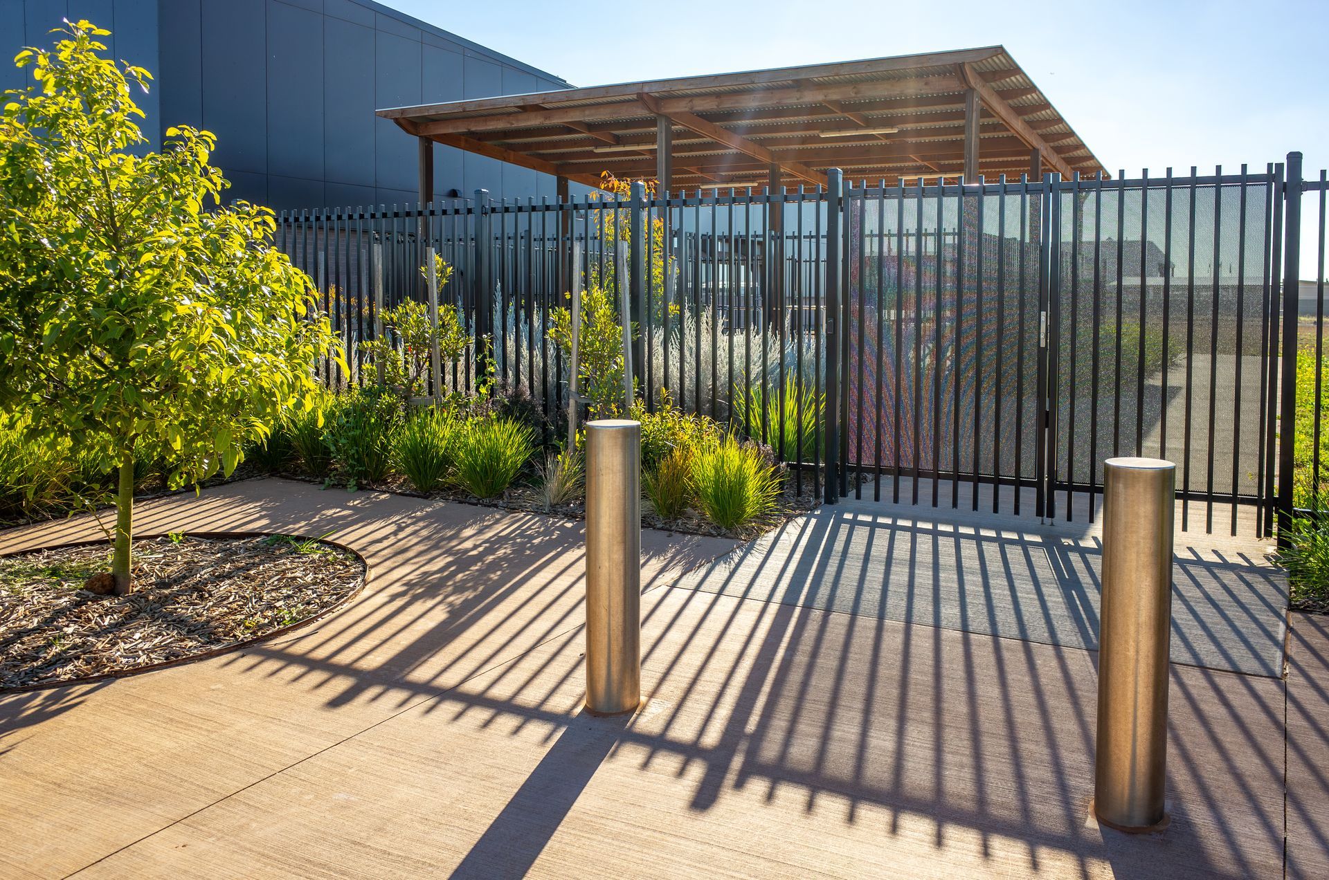 Metal fence casting long shadows near landscaped walkway and building. Metal fence casting long shadows near landscaped walkway and building.